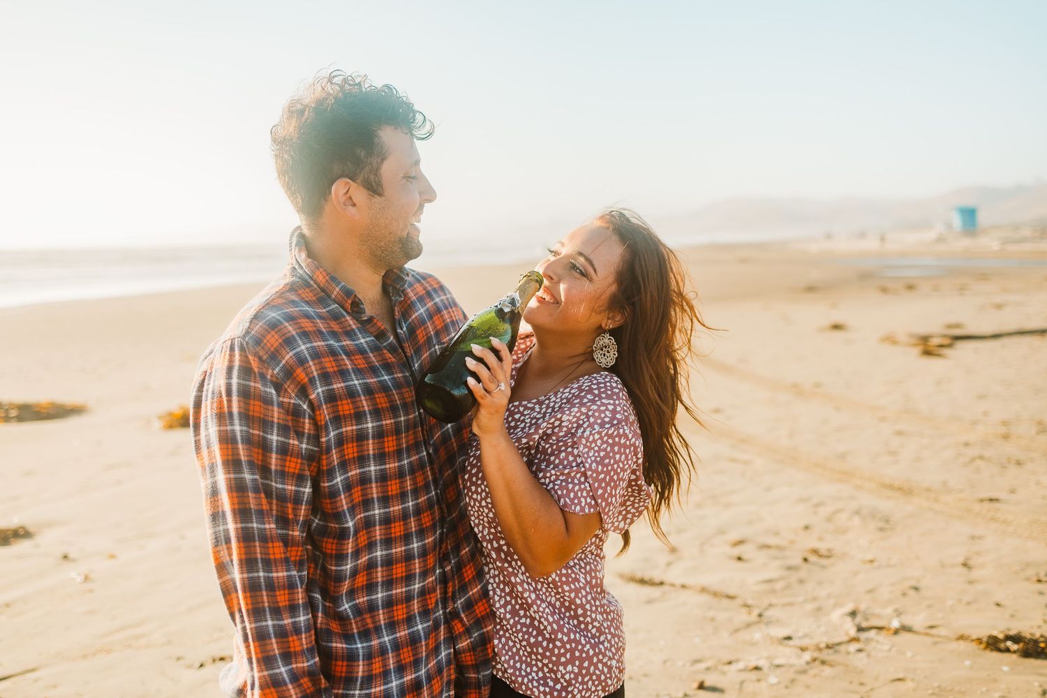 A couple laughs together on a beach during golden hour.