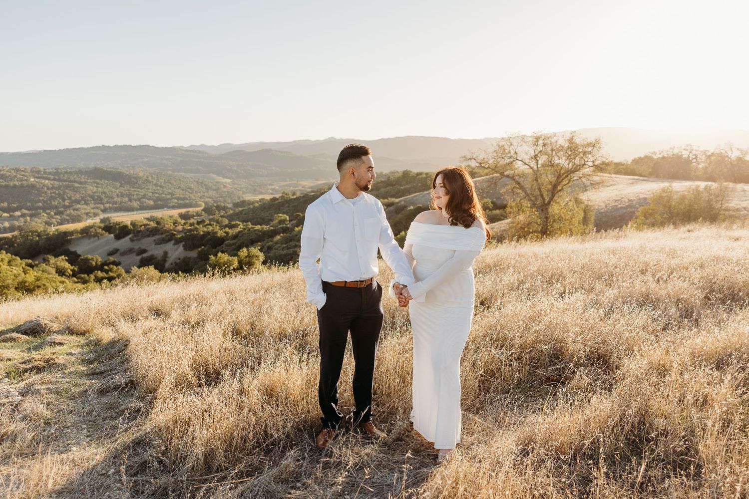 A romantic couple embraces outside a rustic doorway with stone walls and wine barrel decoration.