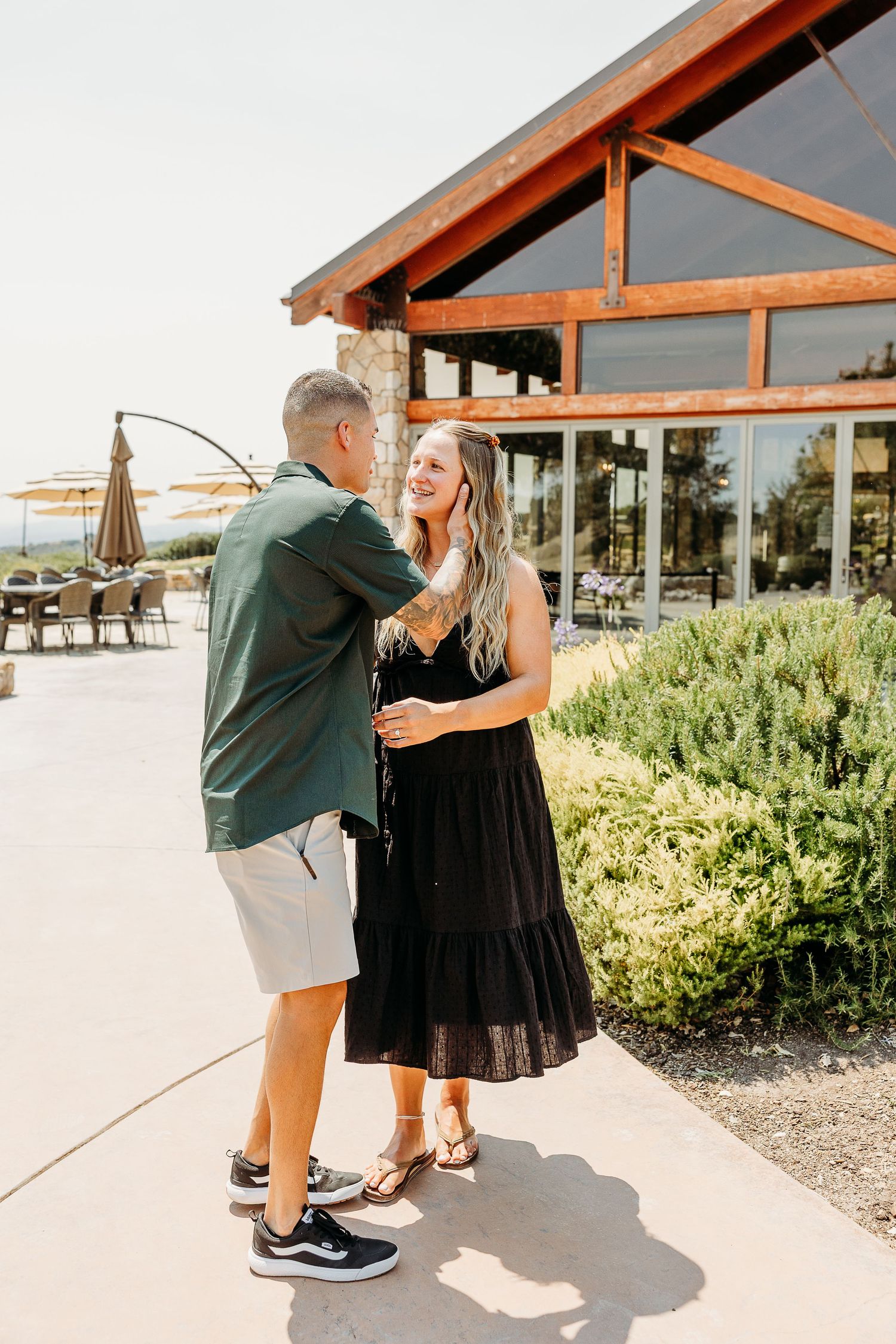 Two people share a tender moment dancing together outside a rustic building with large windows.