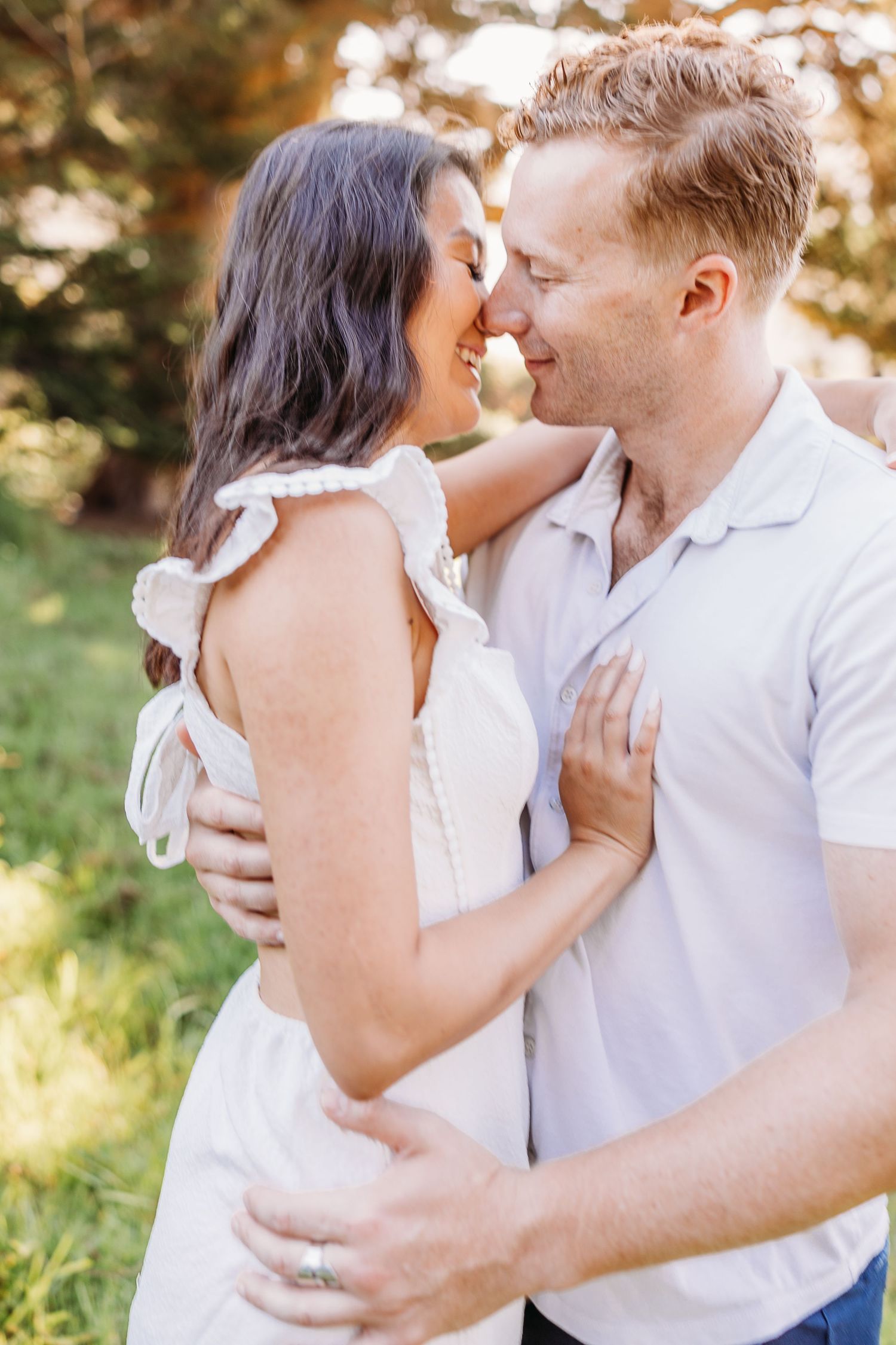 Intimate moment between couple in white outfits against natural outdoor backdrop.