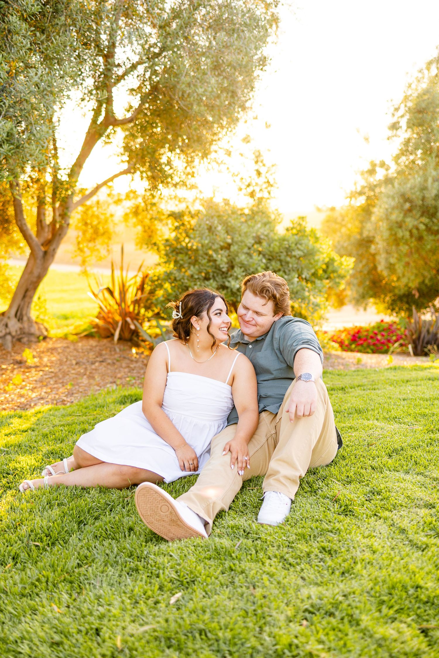 Couple relaxes on grass during golden hour engagement photo session.
