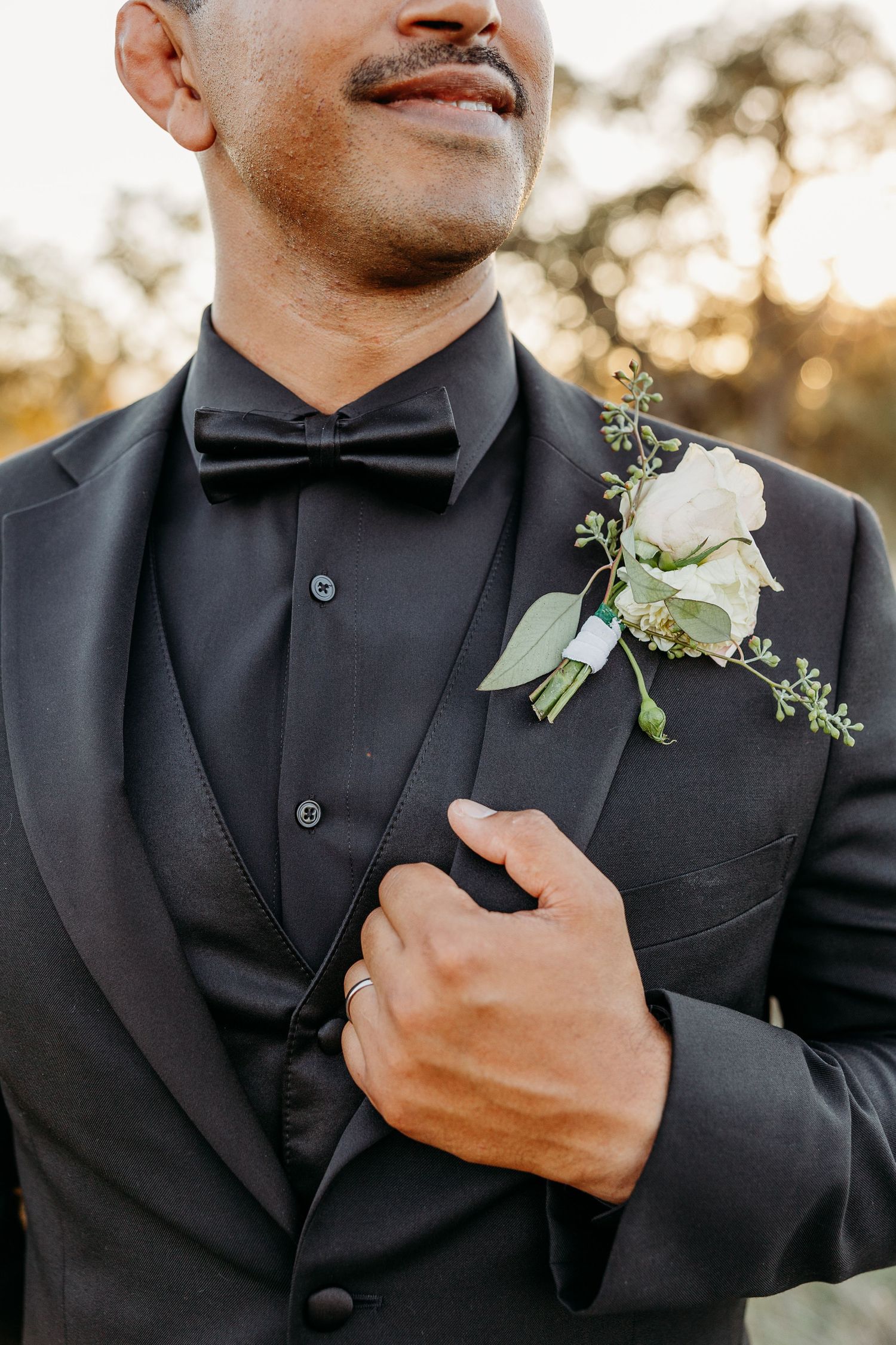 Close-up details of groom's black tuxedo with white boutonniere and bow tie.