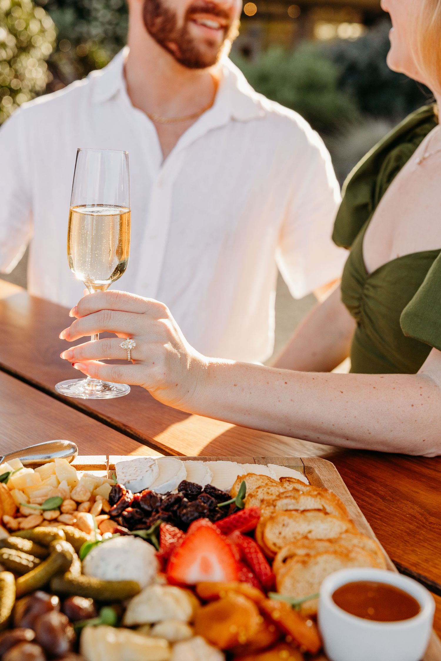 Romantic outdoor dinner setup with wine glasses and appetizer plates on a rustic wooden table at sunset.