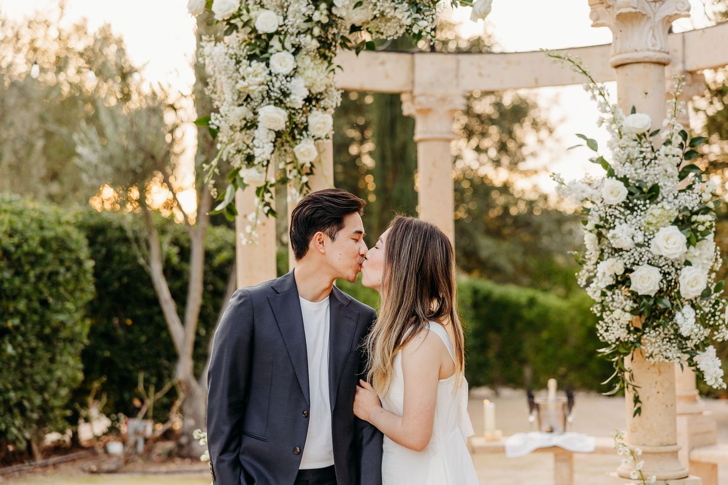 A romantic outdoor scene with white floral decorations and pillars at sunset.