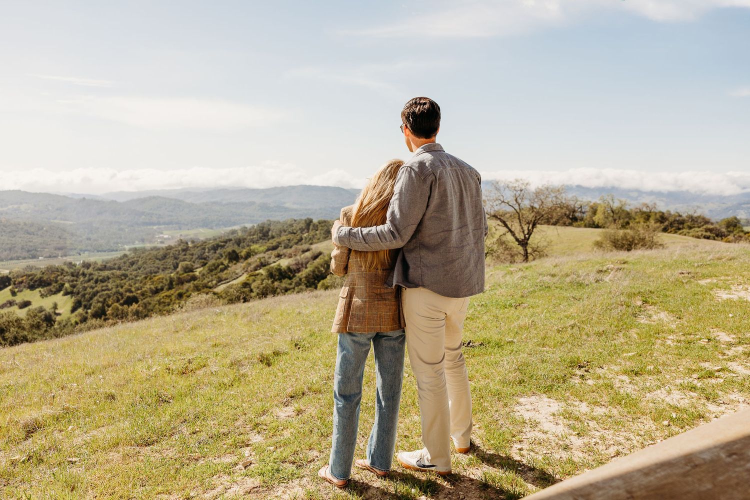 Couple standing together on hilltop overlooking scenic mountain landscape.