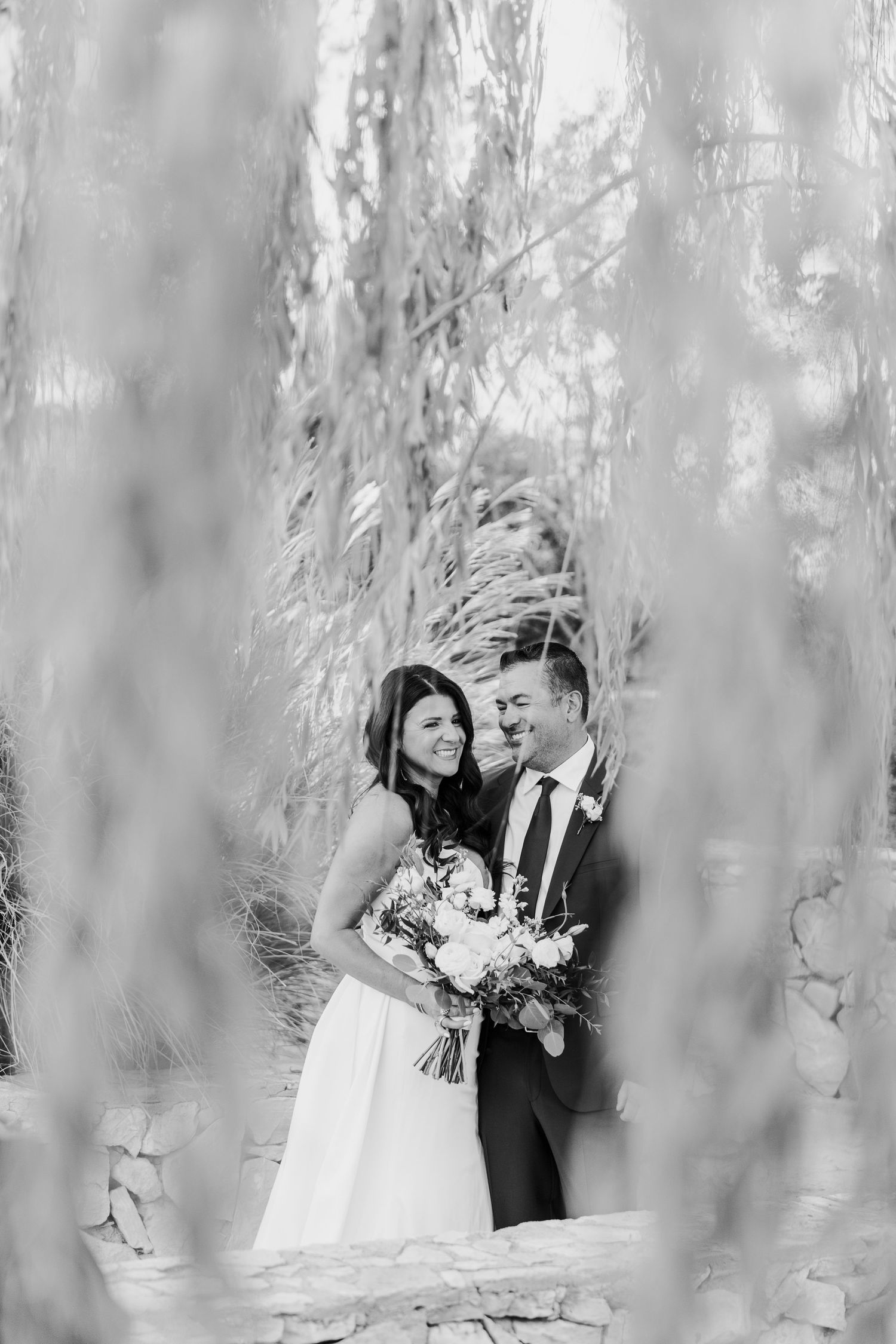 Romantic wedding portraits through willow branches creating a dreamy effect.