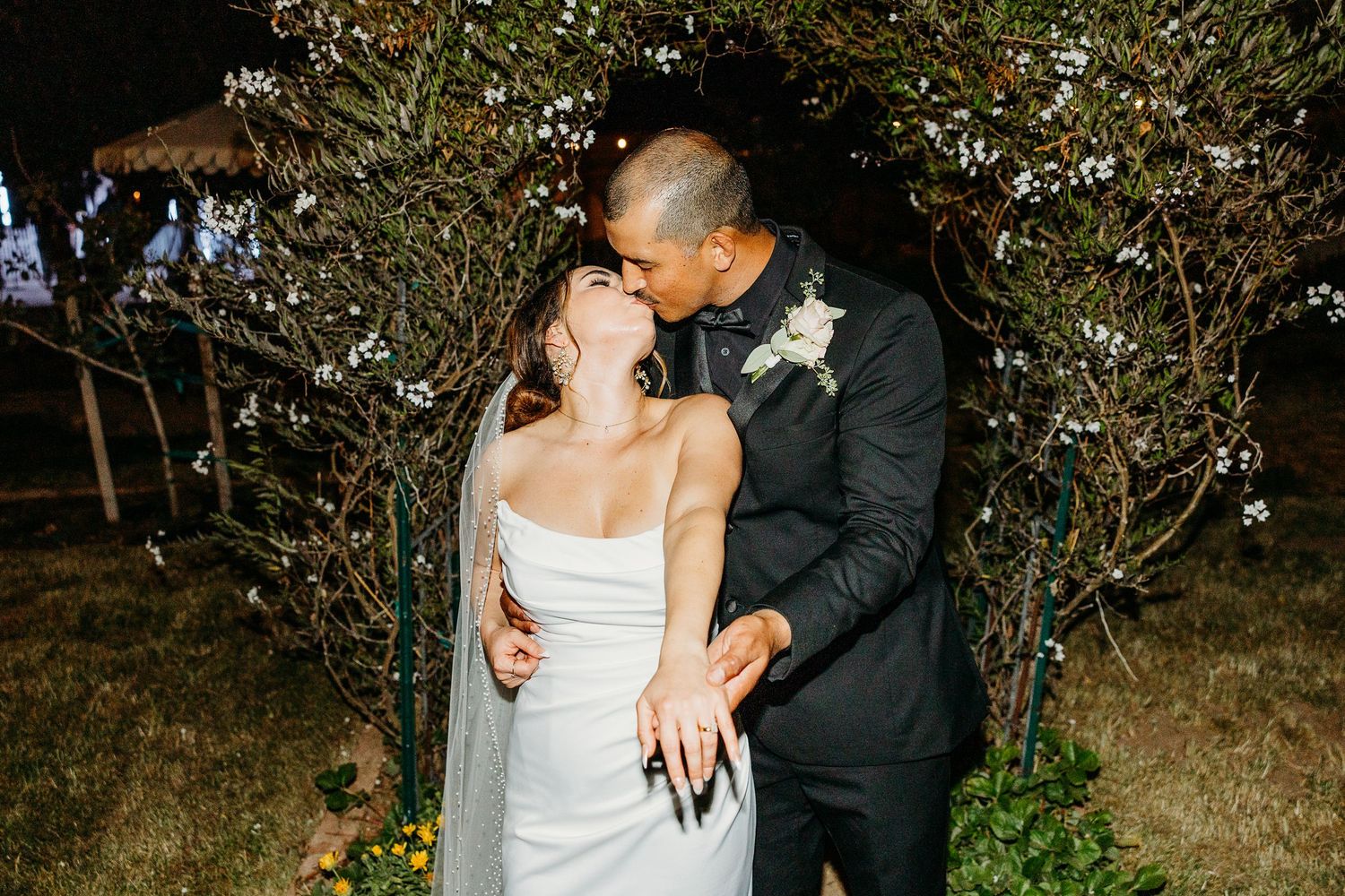 Romantic couple shares intimate moment under flowering trees during evening portraits.