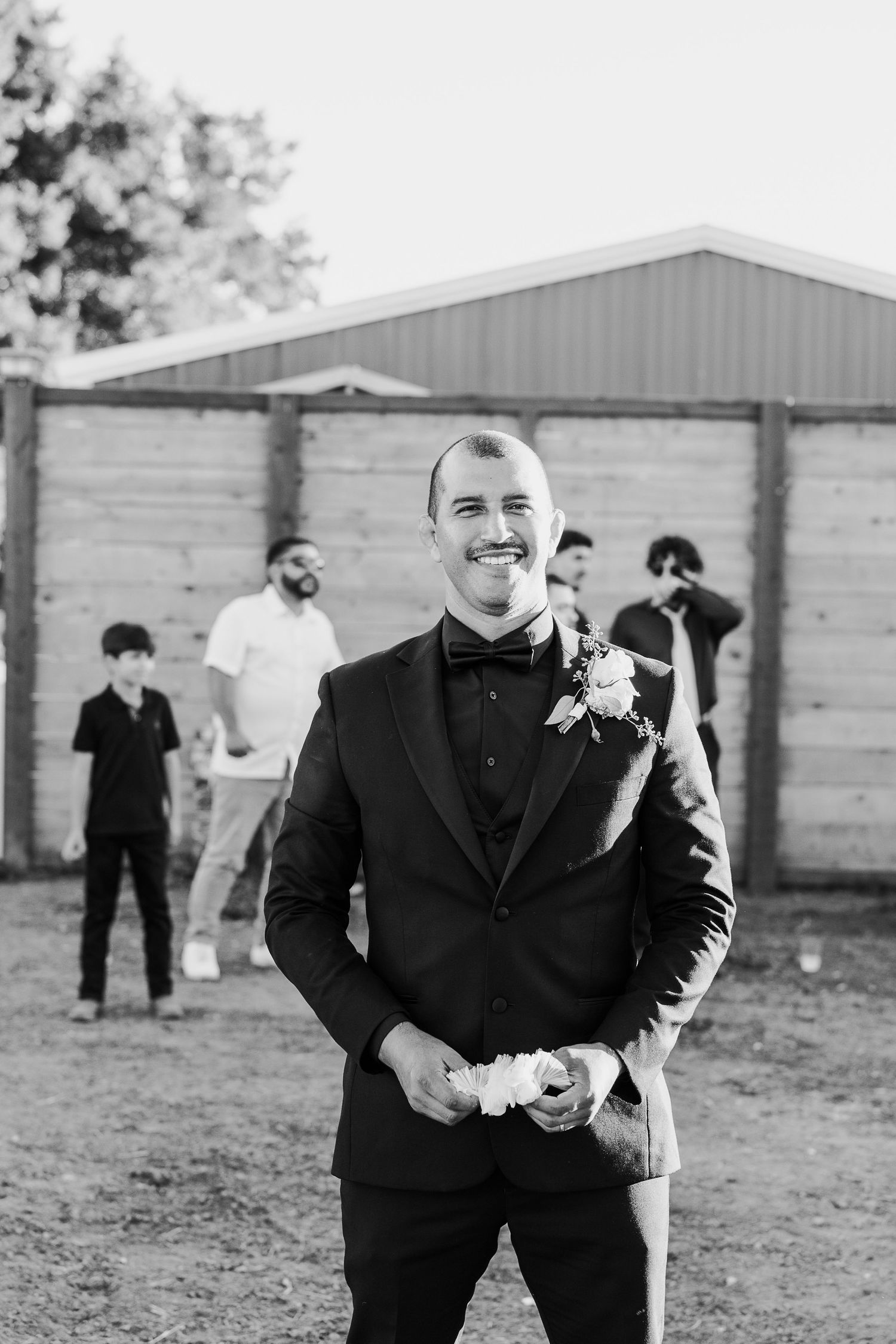 Groomsmen in black suits share laughs during outdoor wedding photo session.