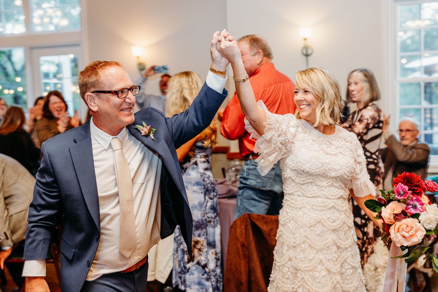 Couple dances joyfully during wedding reception in brightly lit indoor venue.