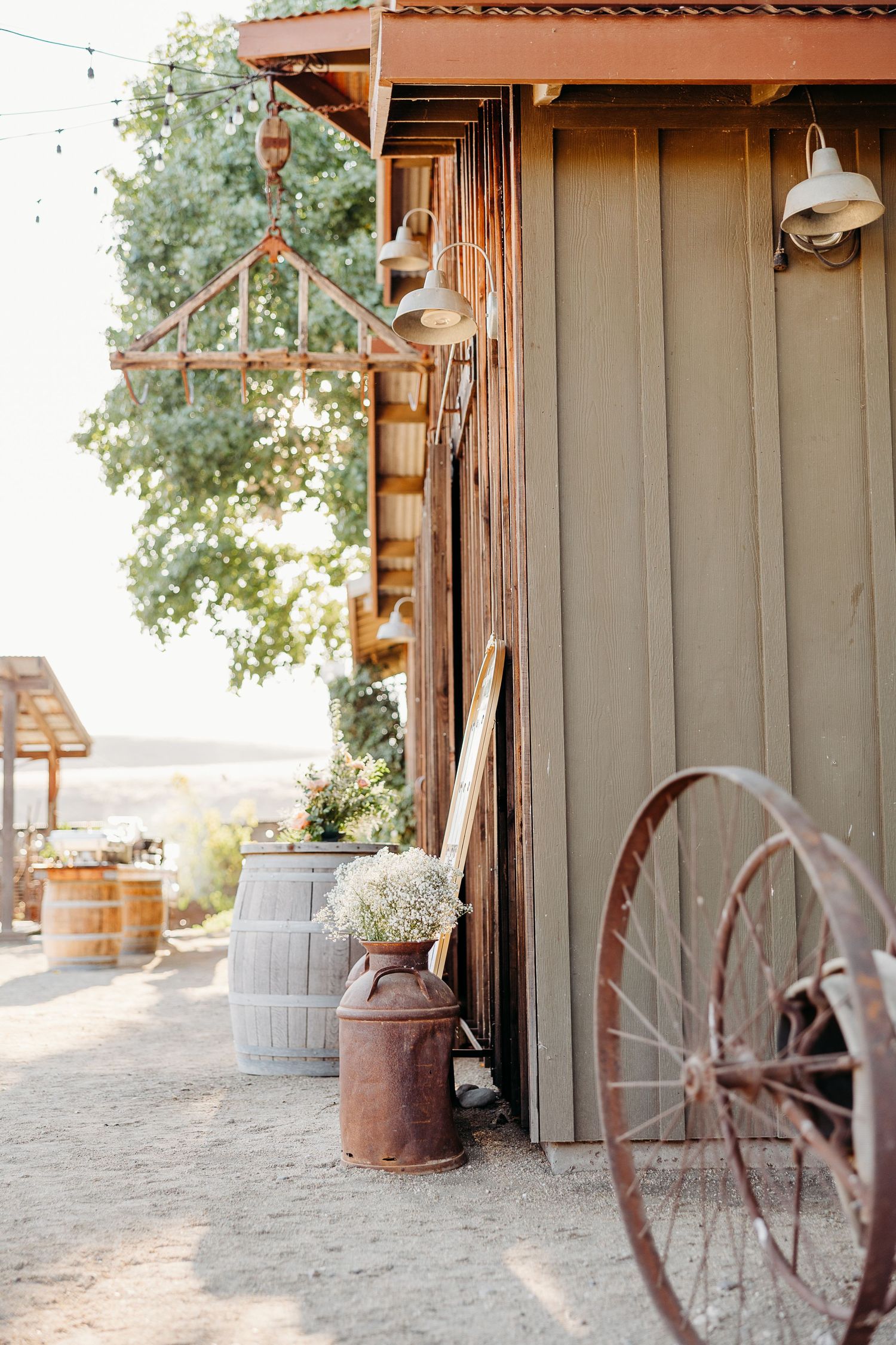 Rustic outdoor venue with milk jugs, wagon wheel, and string lights creating a charming country atmosphere.