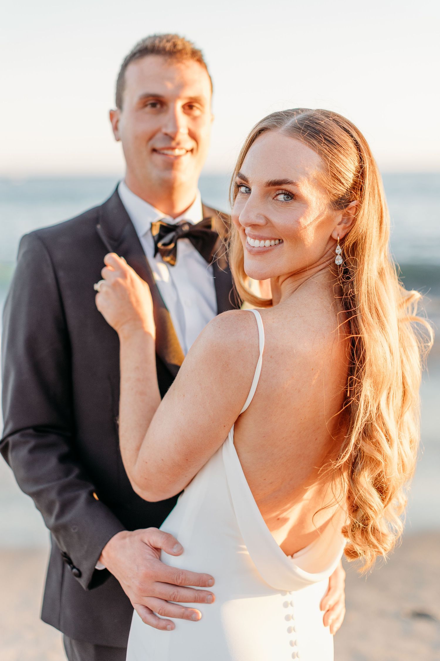 Candid beach portraits of bride and groom laughing together during golden hour.