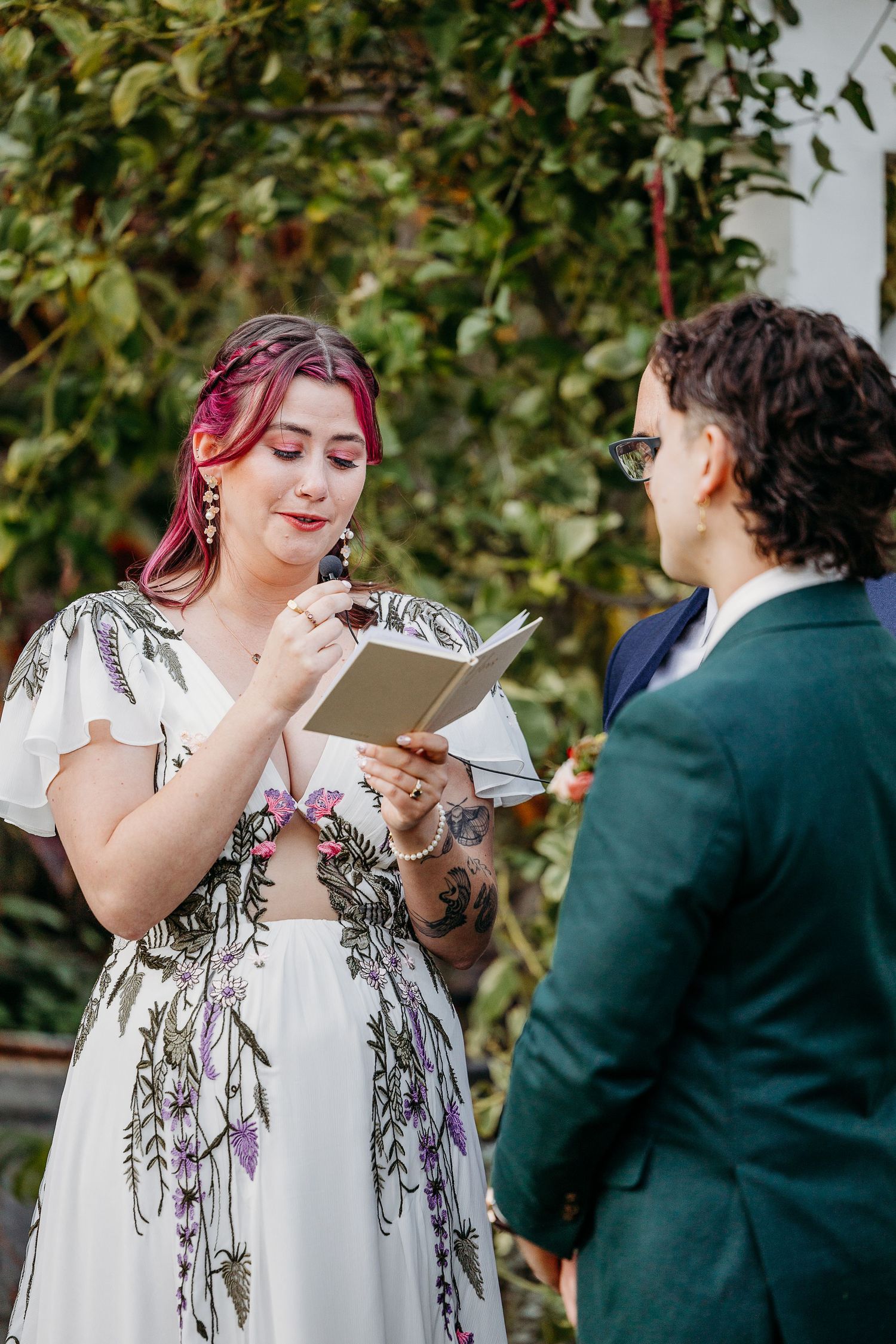 A person in a white floral dress reads from papers during an outdoor ceremony.