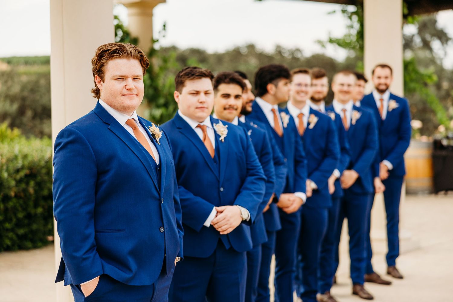Wedding party wearing coordinated blue suits lined up at an outdoor ceremony venue.