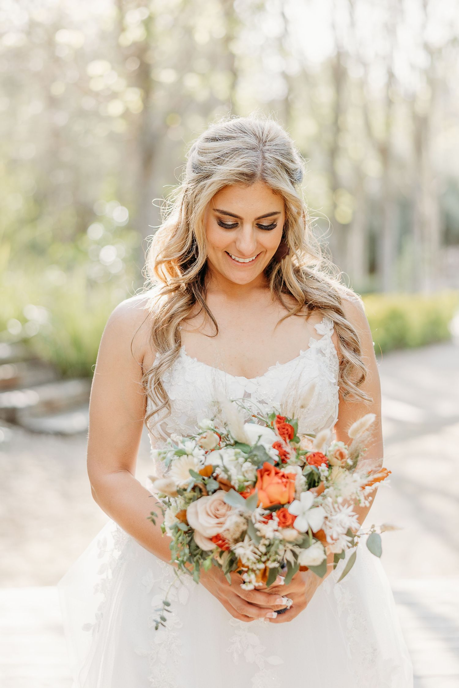 A bride holds a beautiful coral and white bouquet against her lace wedding dress.