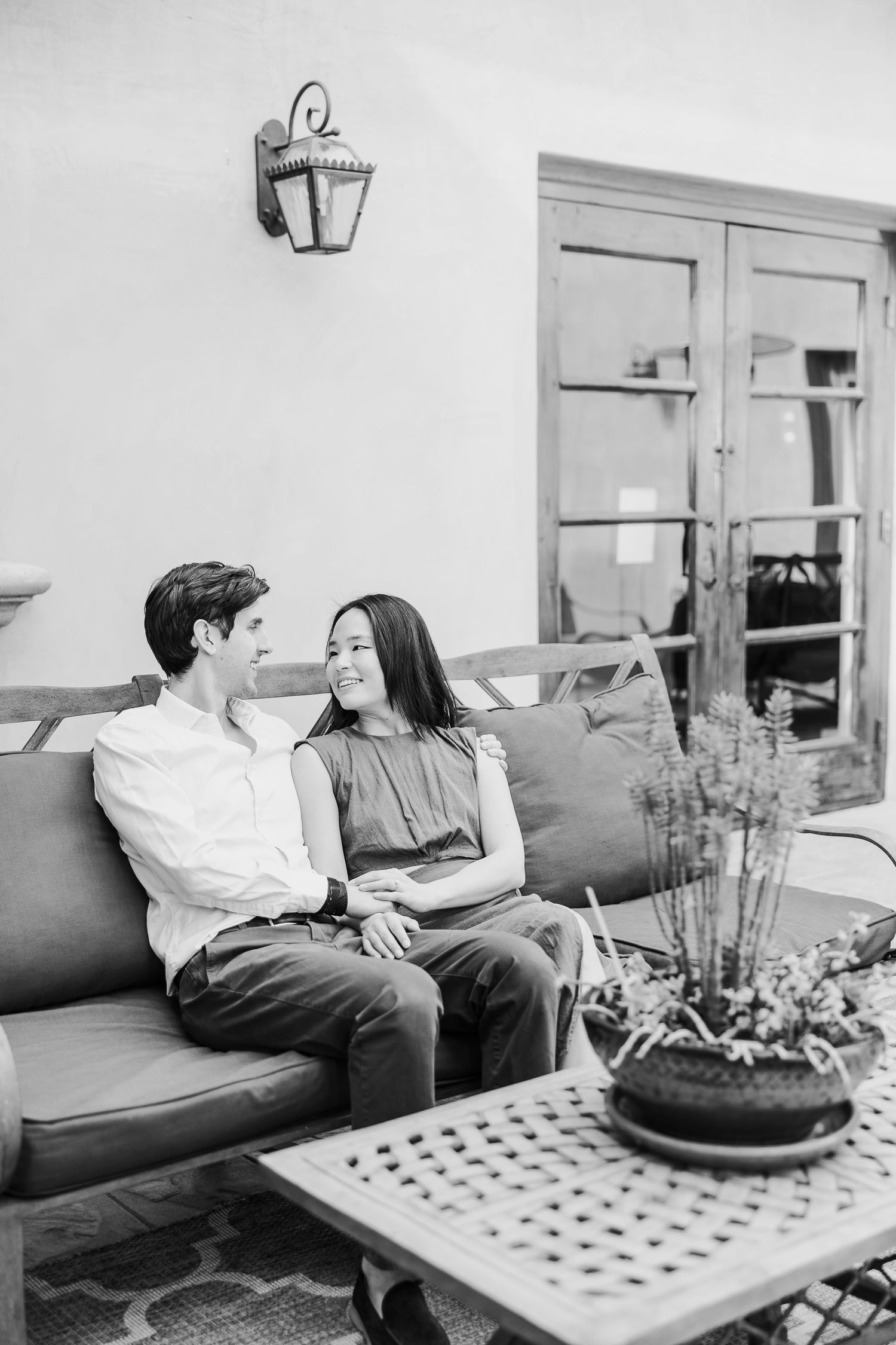 A romantic black and white moment of a couple sharing an intimate conversation on a couch with a potted plant nearby.