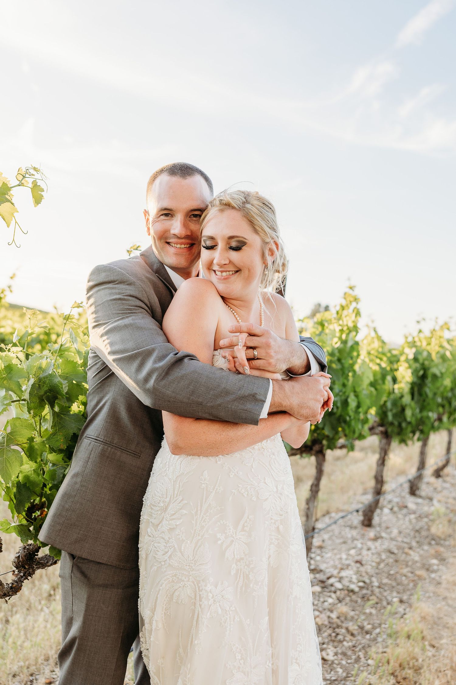 A joyful embrace between newlyweds in a vineyard setting on their wedding day.