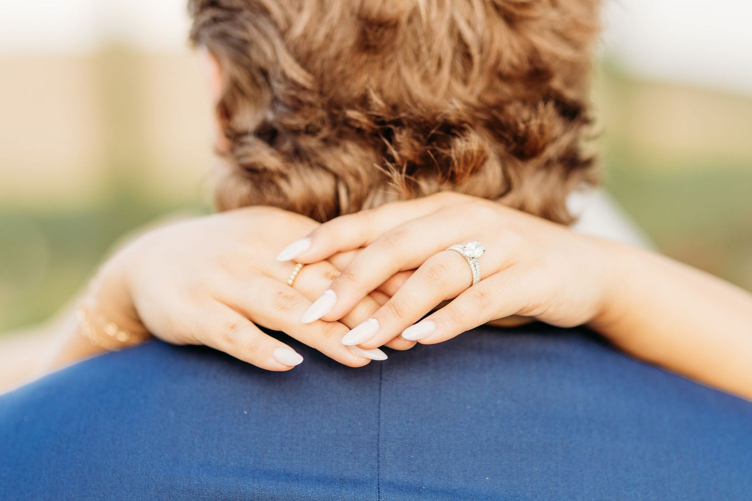 Close-up of hands with engagement ring resting on shoulder during romantic wedding embrace.