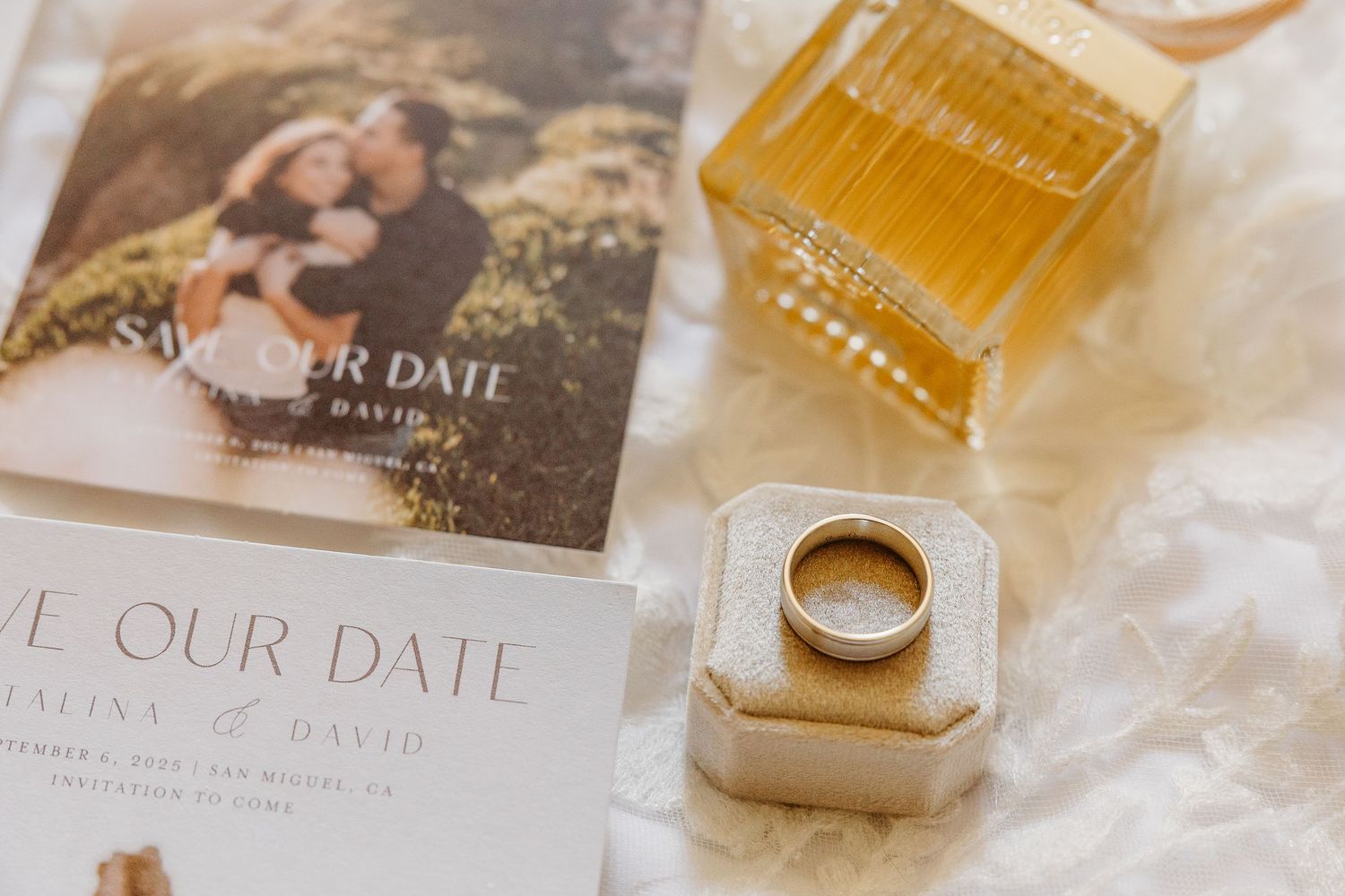 Wedding detail flatlay with invitations, rings, perfume bottles, and decorative elements in soft neutral tones.