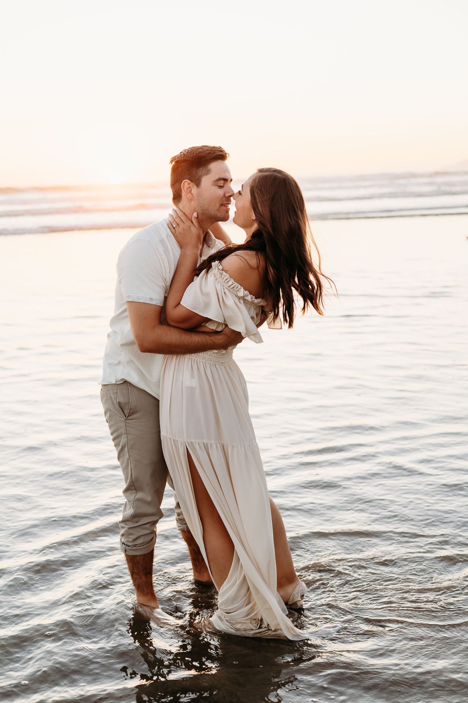 Romantic embrace in ocean waves with sunset lighting and coastal background.