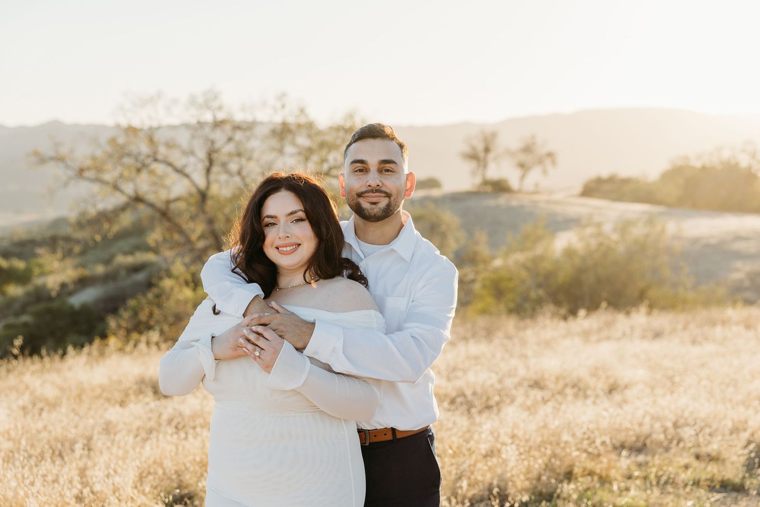 Happy couple embracing in a golden field at sunset wearing coordinated white and blue outfits.