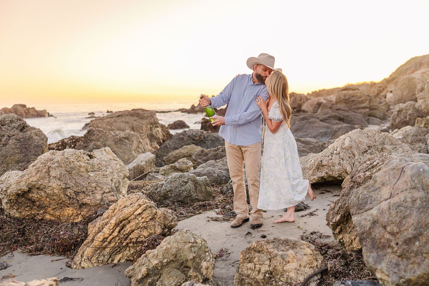 A romantic sunset beach moment as a couple stands among rocky coastal formations.