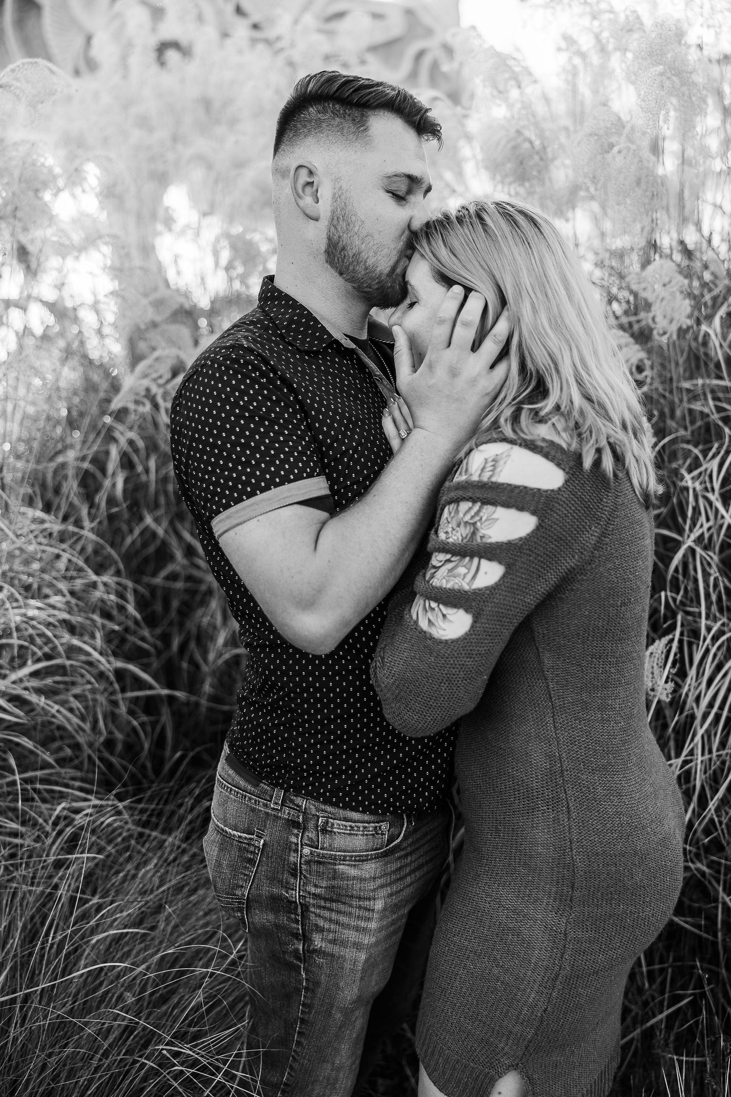 A black and white intimate portrait of a couple embracing among tall grasses.
