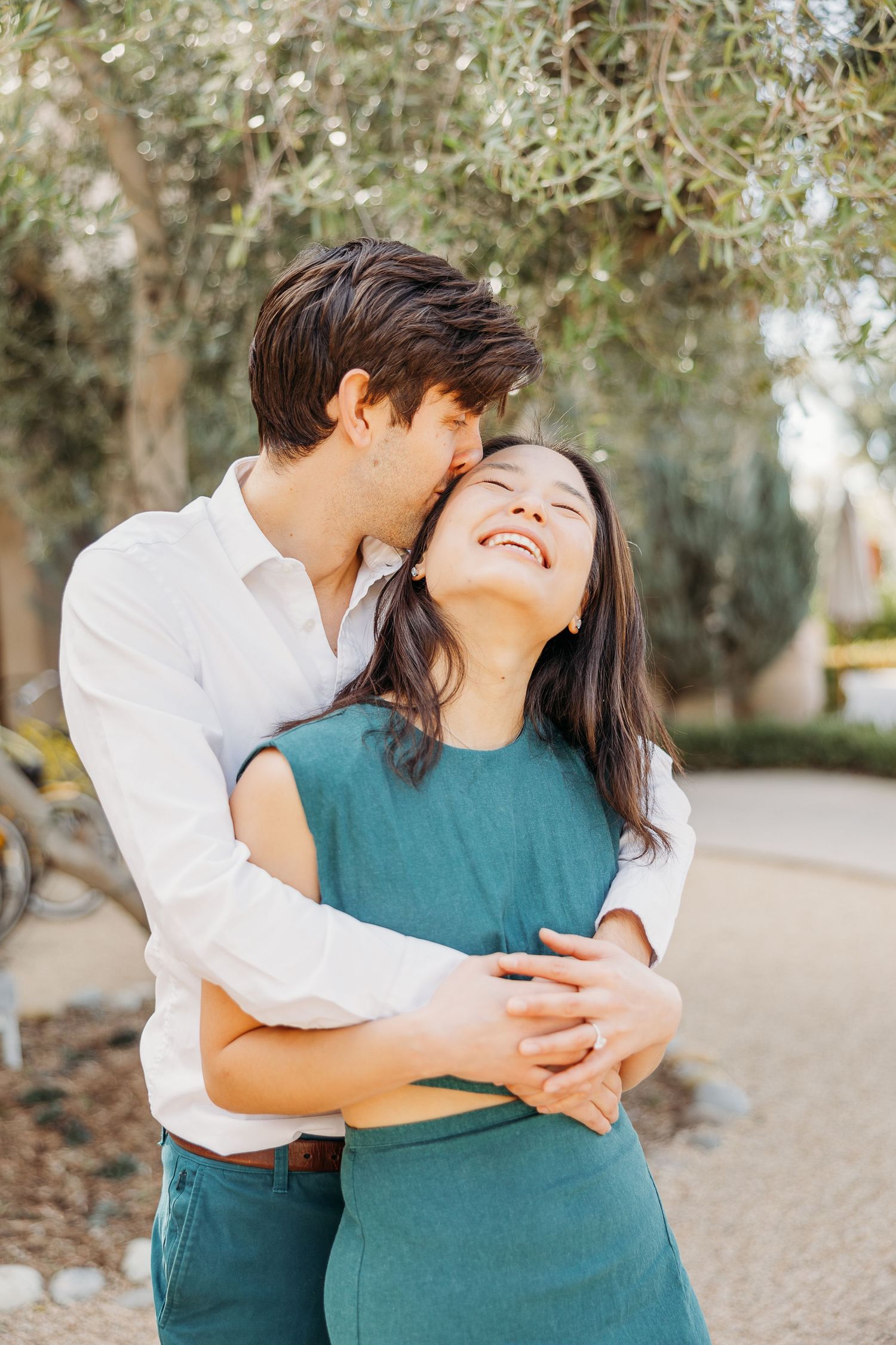 Couple sharing a tender romantic moment outdoors, embracing and smiling while wearing coordinated teal and white outfits.