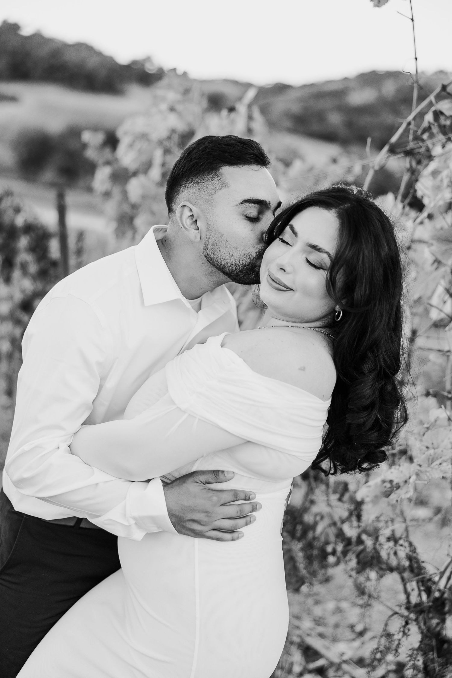 An intimate black and white photo of a couple sharing a tender moment among nature.