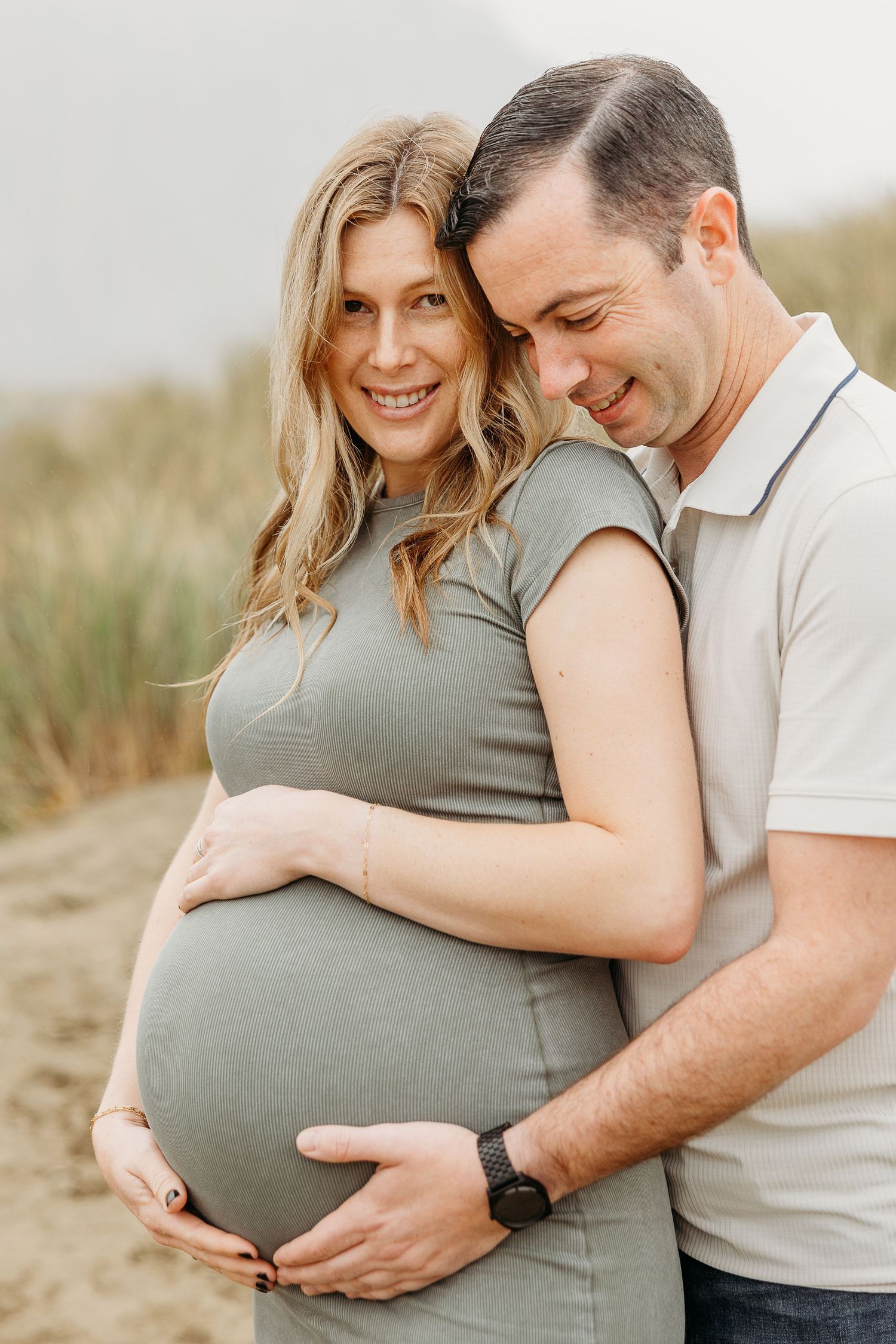 Joyful maternity portrait with couple embracing and cradling baby bump outdoors.
