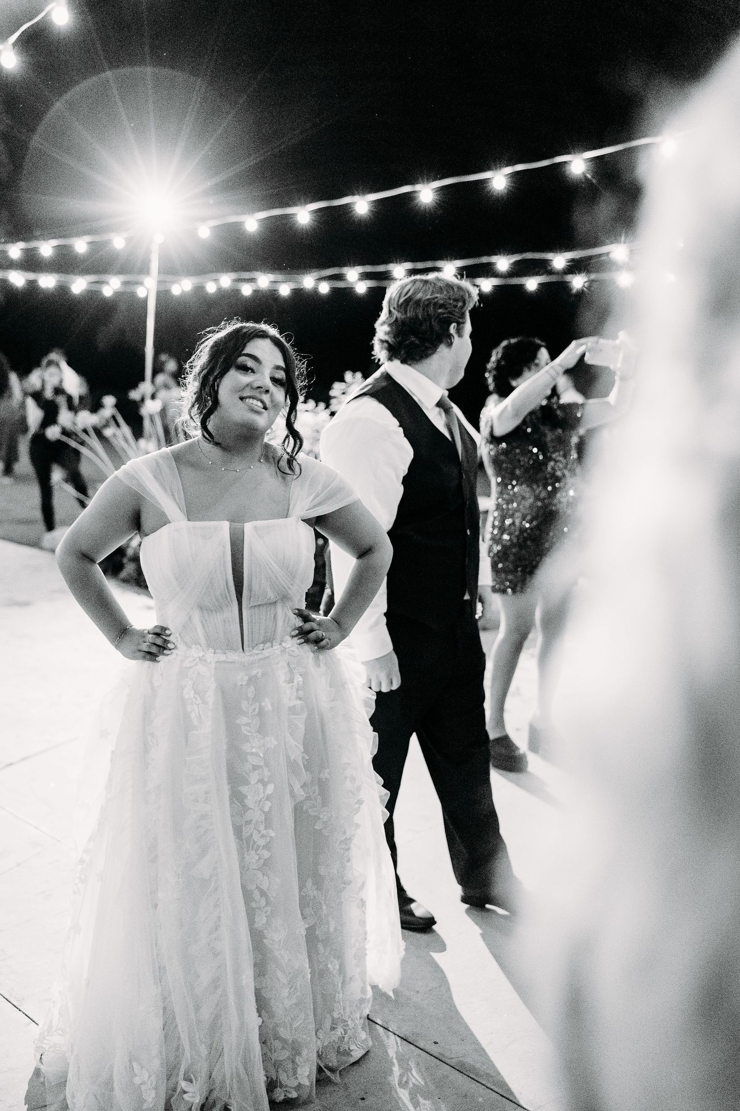 Couple enjoying their wedding reception under twinkling string lights at an outdoor evening celebration.