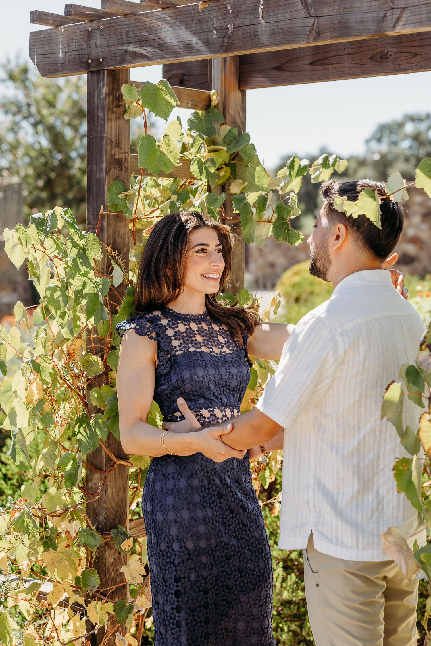 Couple sharing a moment under a wooden pergola covered in climbing vines.