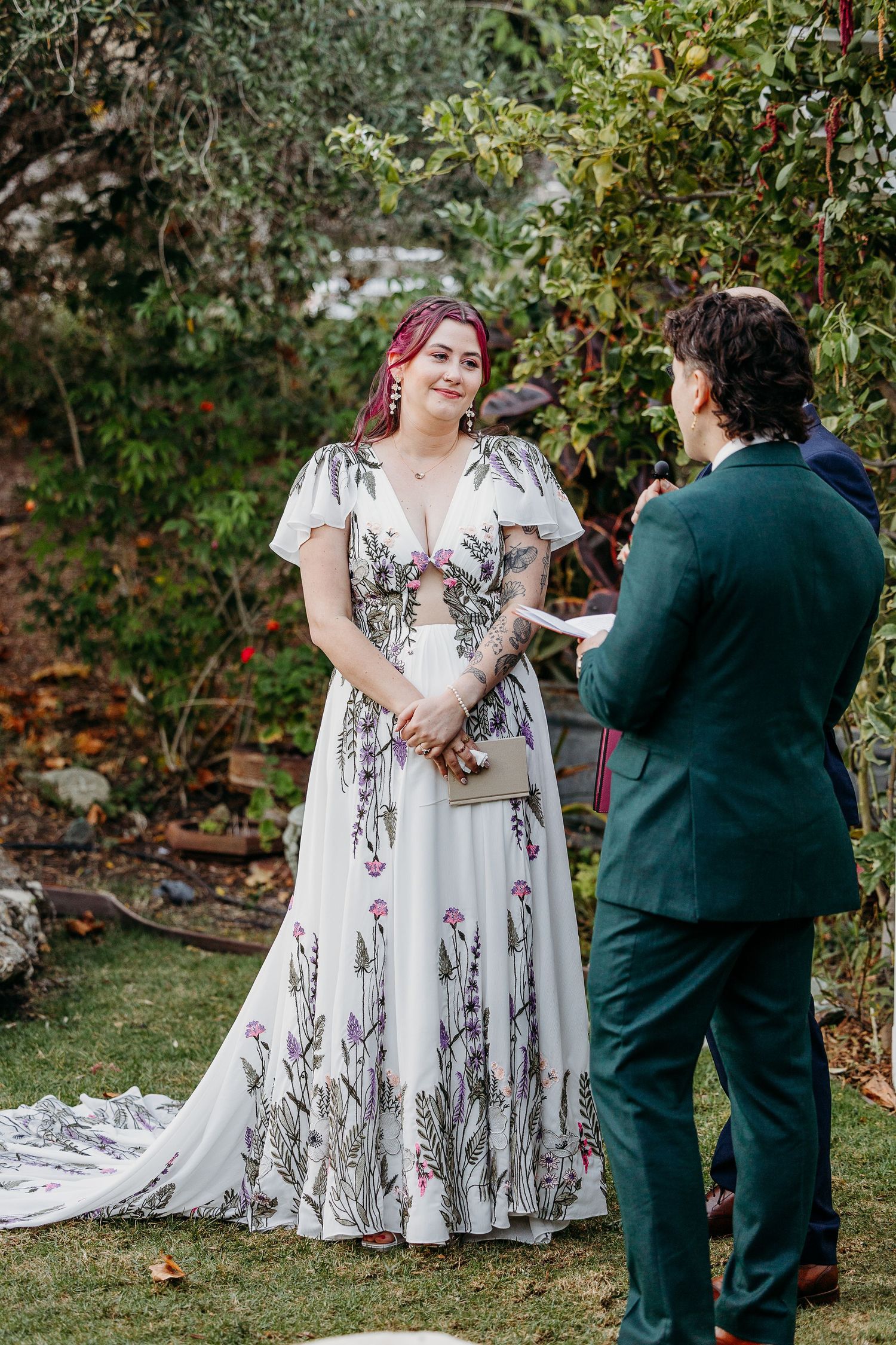 A couple shares a tender moment outdoors during their wedding ceremony, with the bride wearing a floral embroidered gown.