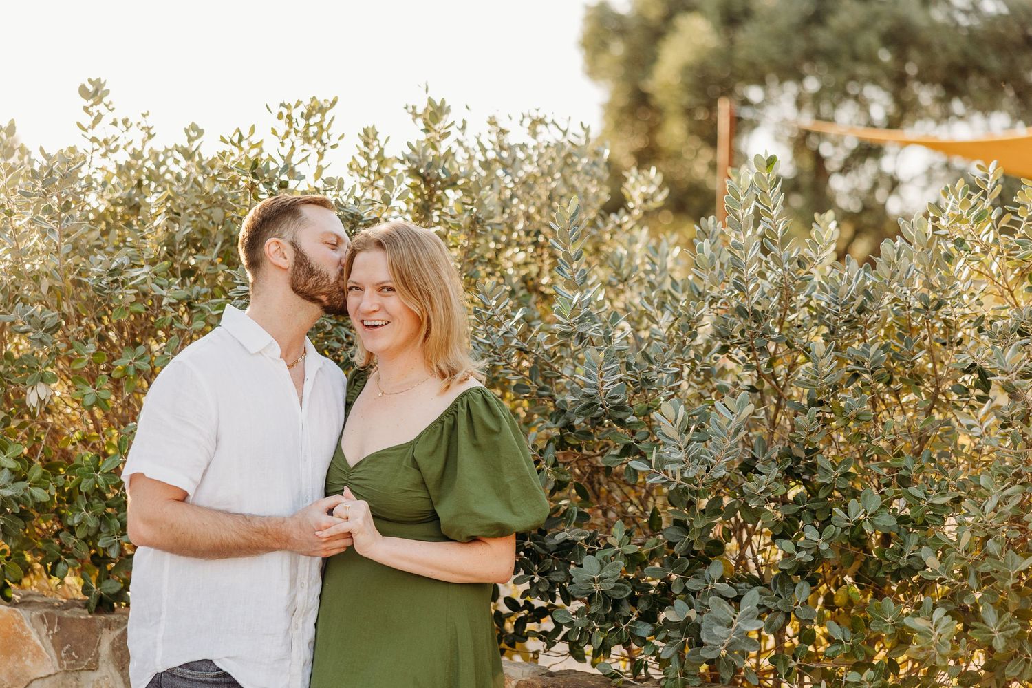 Romantic couple sharing tender moment among flowering bushes at sunset.