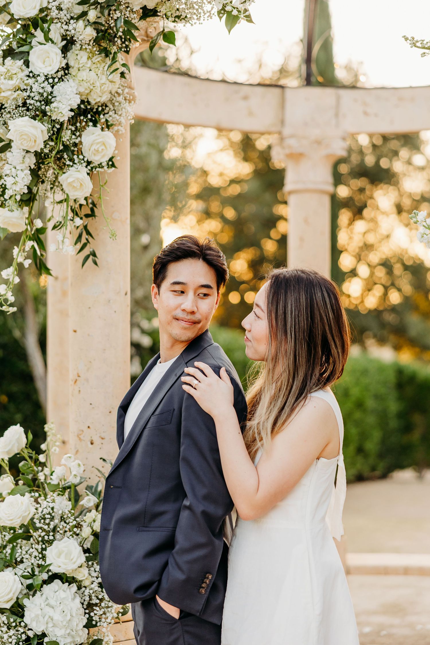 Couple sharing intimate moments under a floral-decorated gazebo during sunset.
