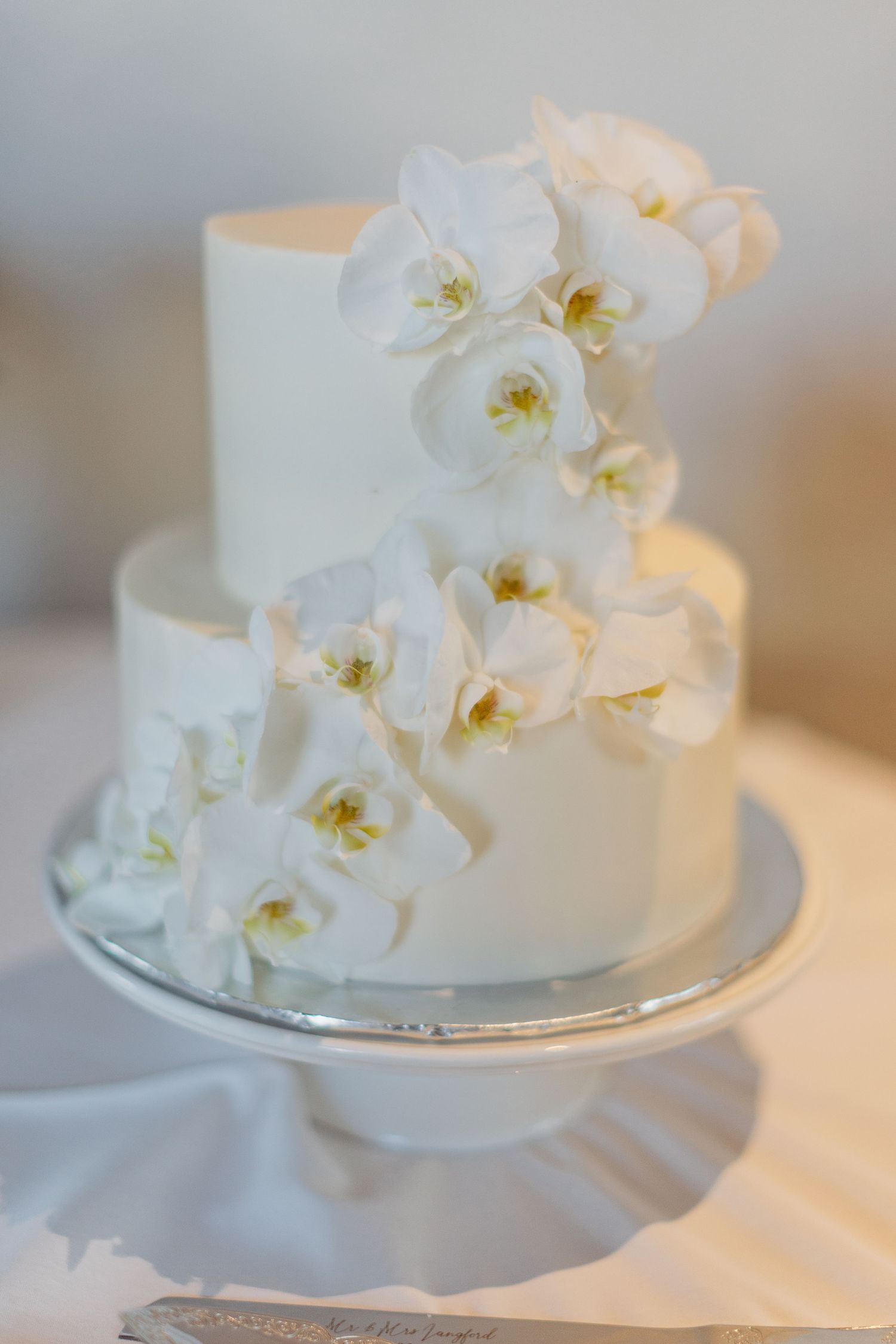 Elegant white wedding cake decorated with delicate white orchids on a silver cake stand.