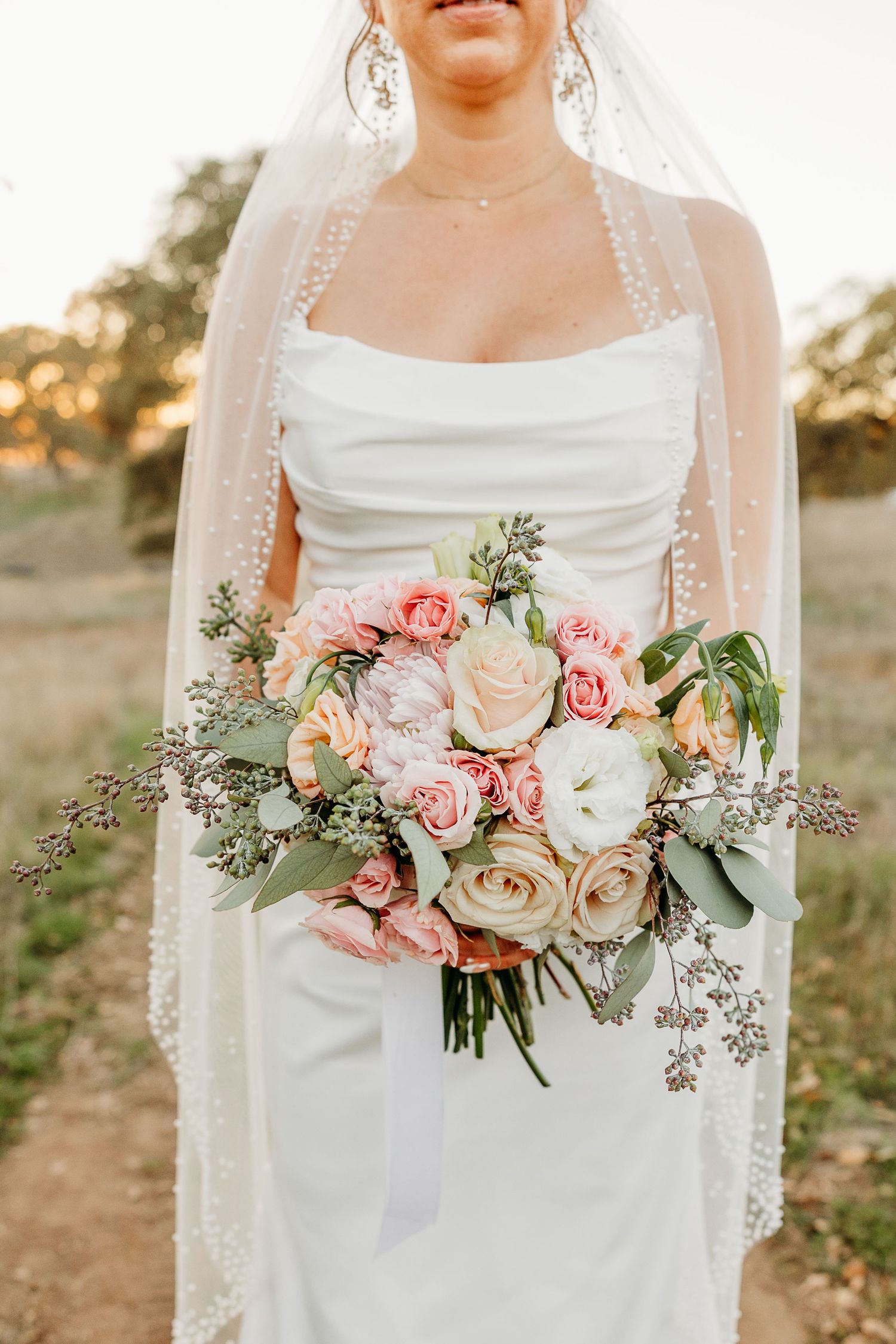 Close-up of bridal bouquet with pink roses and greenery against outdoor background.