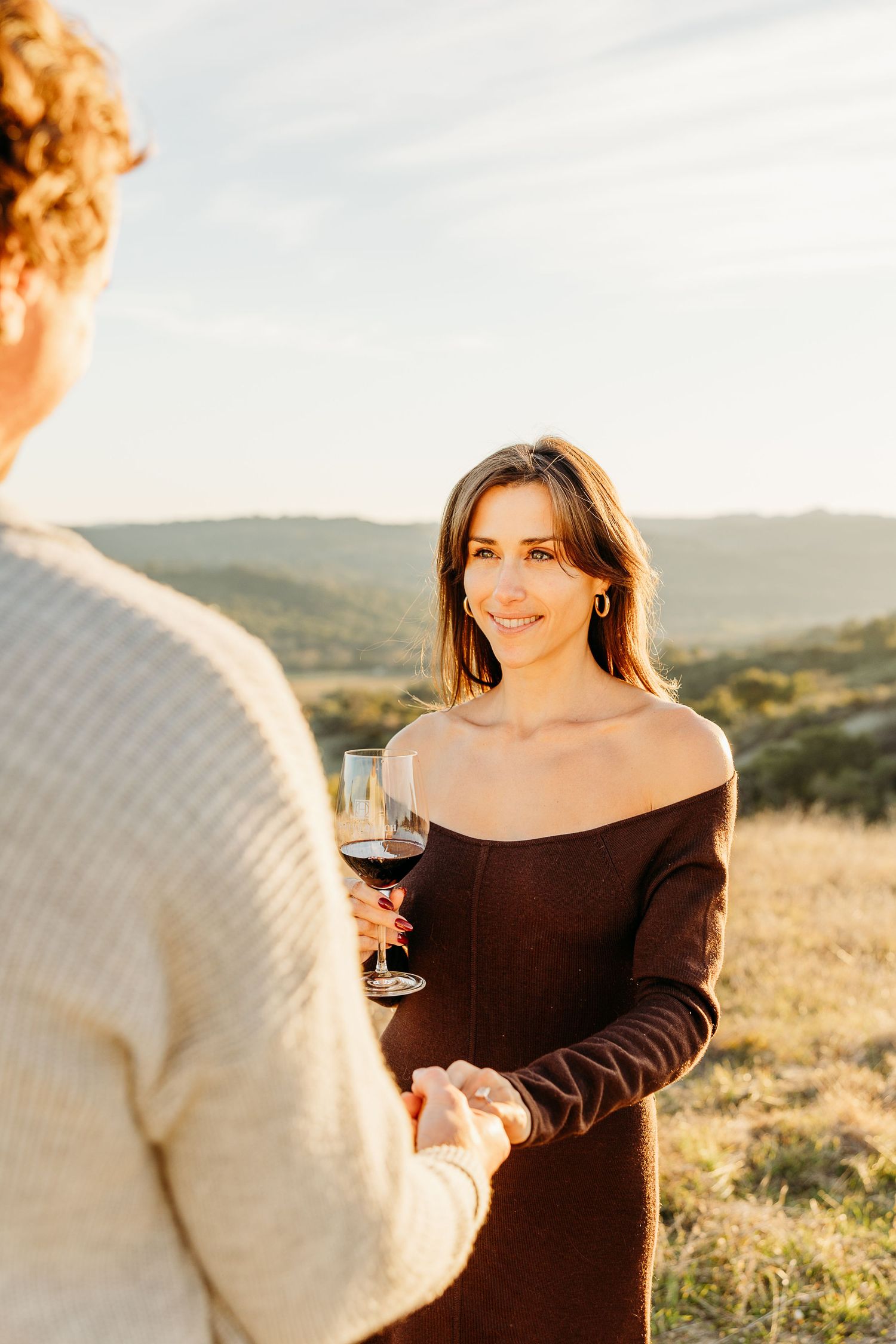 Couple enjoying wine together in scenic countryside setting during sunset.
