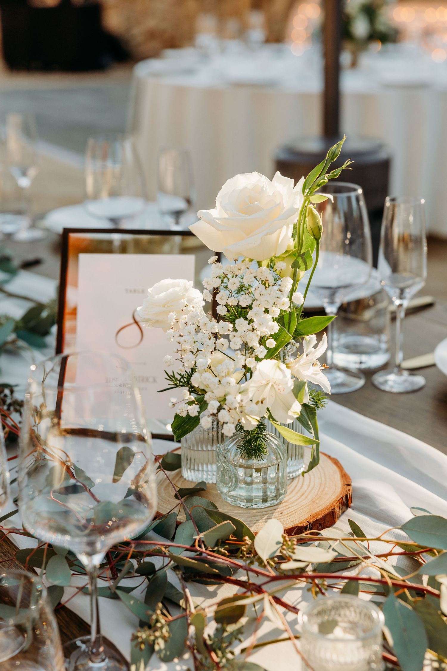 Elegant wedding reception table setting with white flowers, greenery and crystal glassware on white linens.