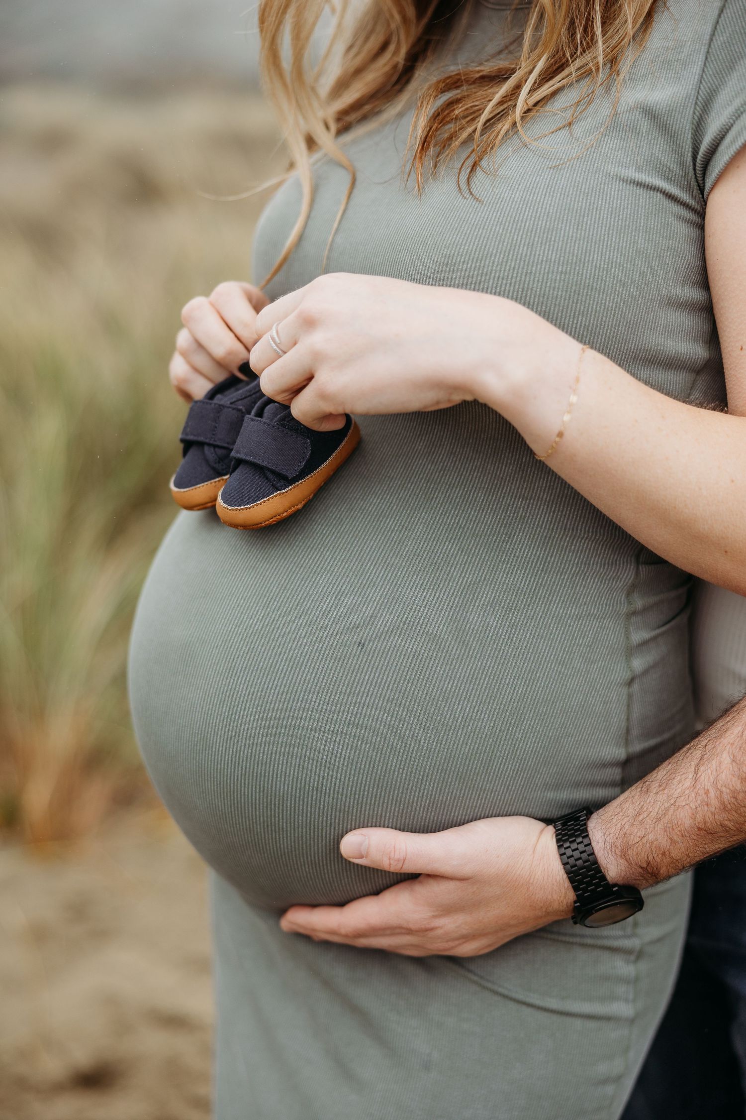 Close up of baby shoes held against pregnant belly with supporting hand.
