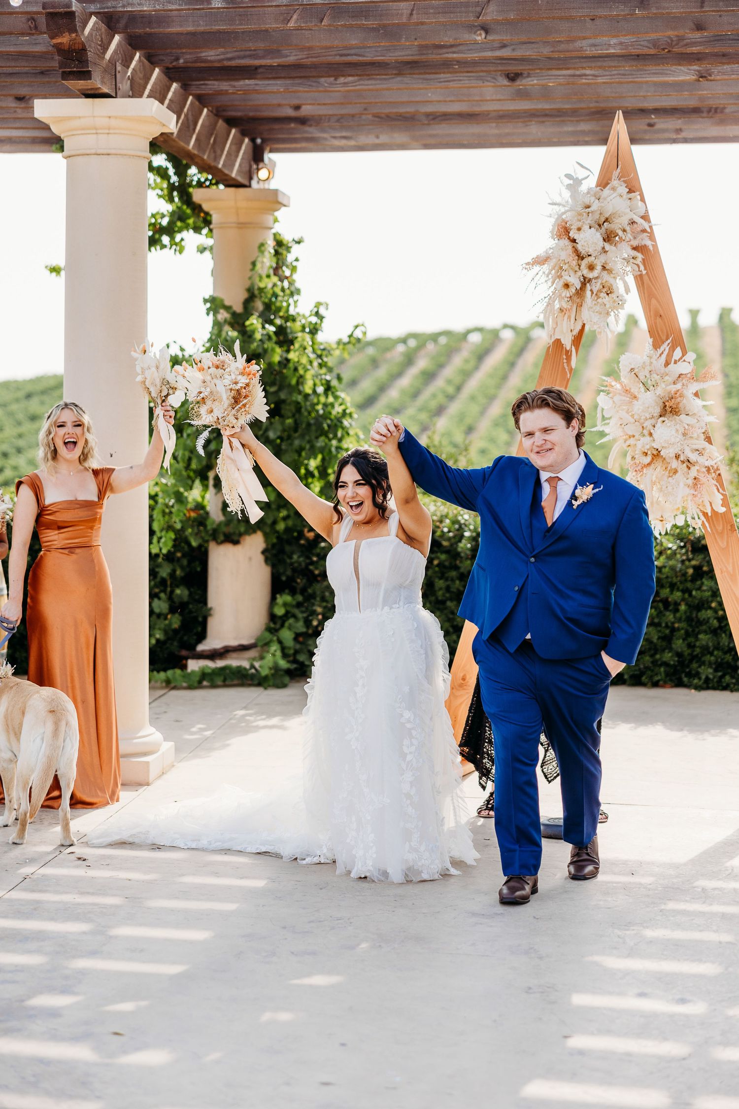 Newlyweds celebrate their wedding ceremony exit at a winery with bridesmaids and floral decorations.
