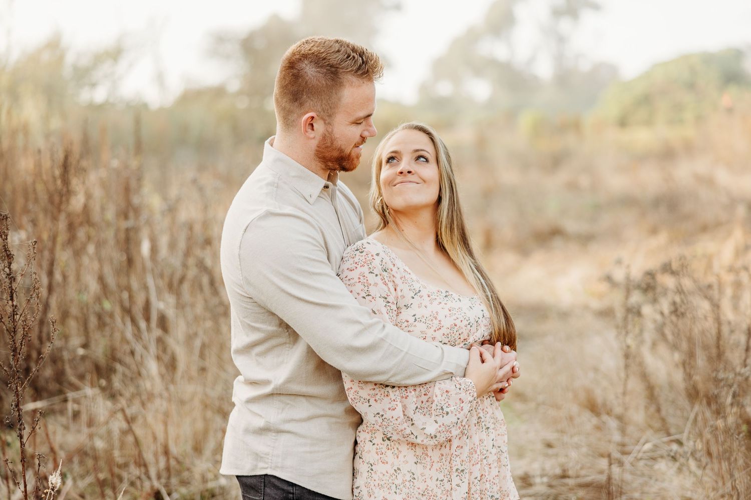 Couple embraces in golden field during sunset photo session.
