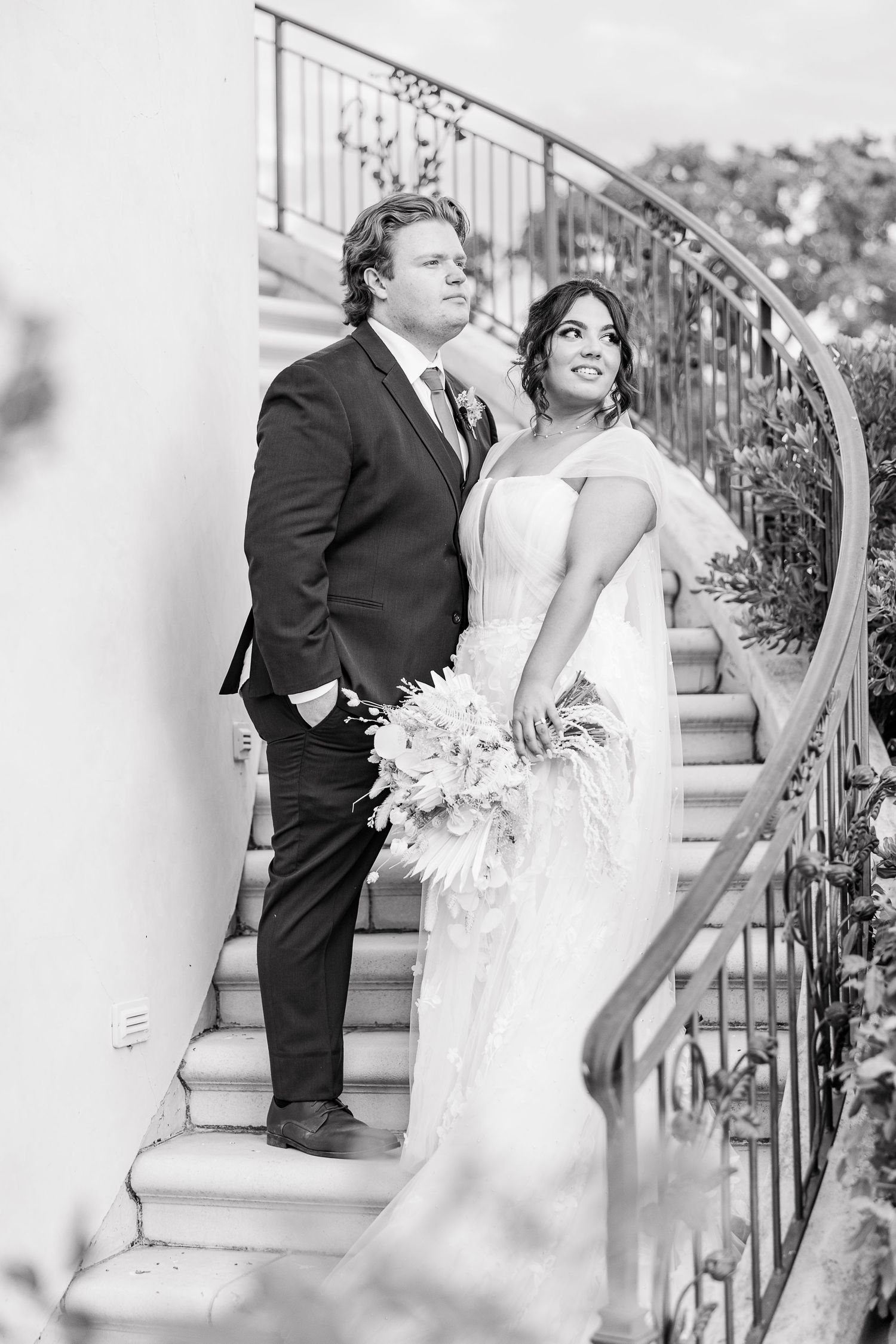 A black and white portrait of newlyweds posing on curved stairs with ornate railings.