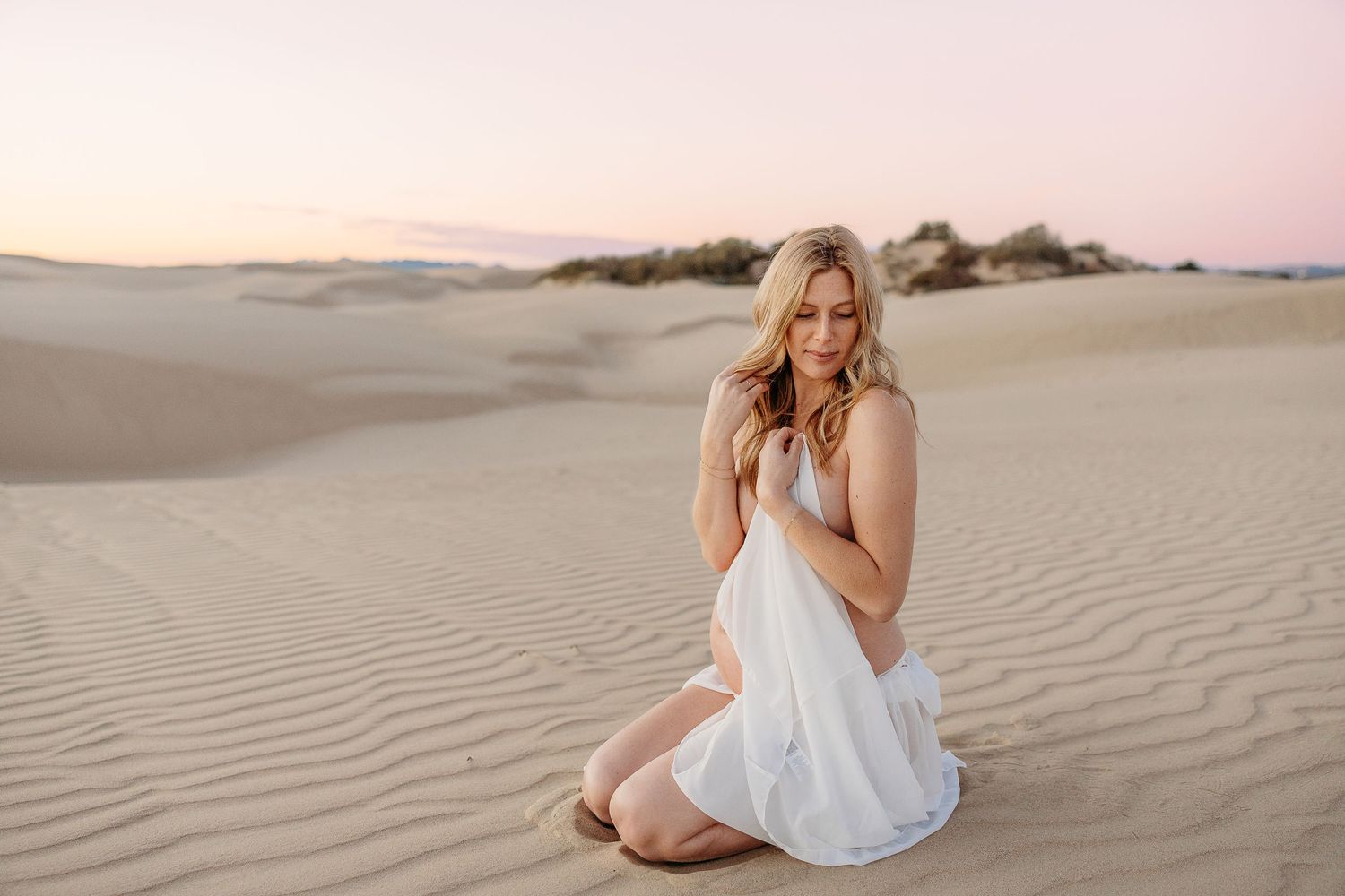 Romantic desert maternity portrait during golden hour with white dress.