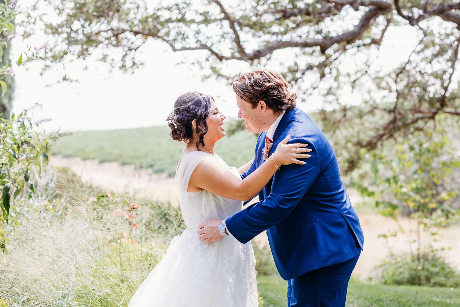 A couple embraces outdoors during their romantic wedding ceremony surrounded by nature.