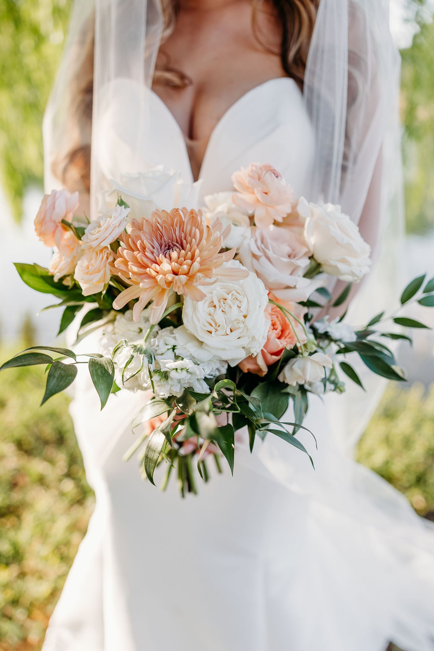 Close-up of peach and white wedding bouquets with roses, dahlias, and greenery against a white dress.