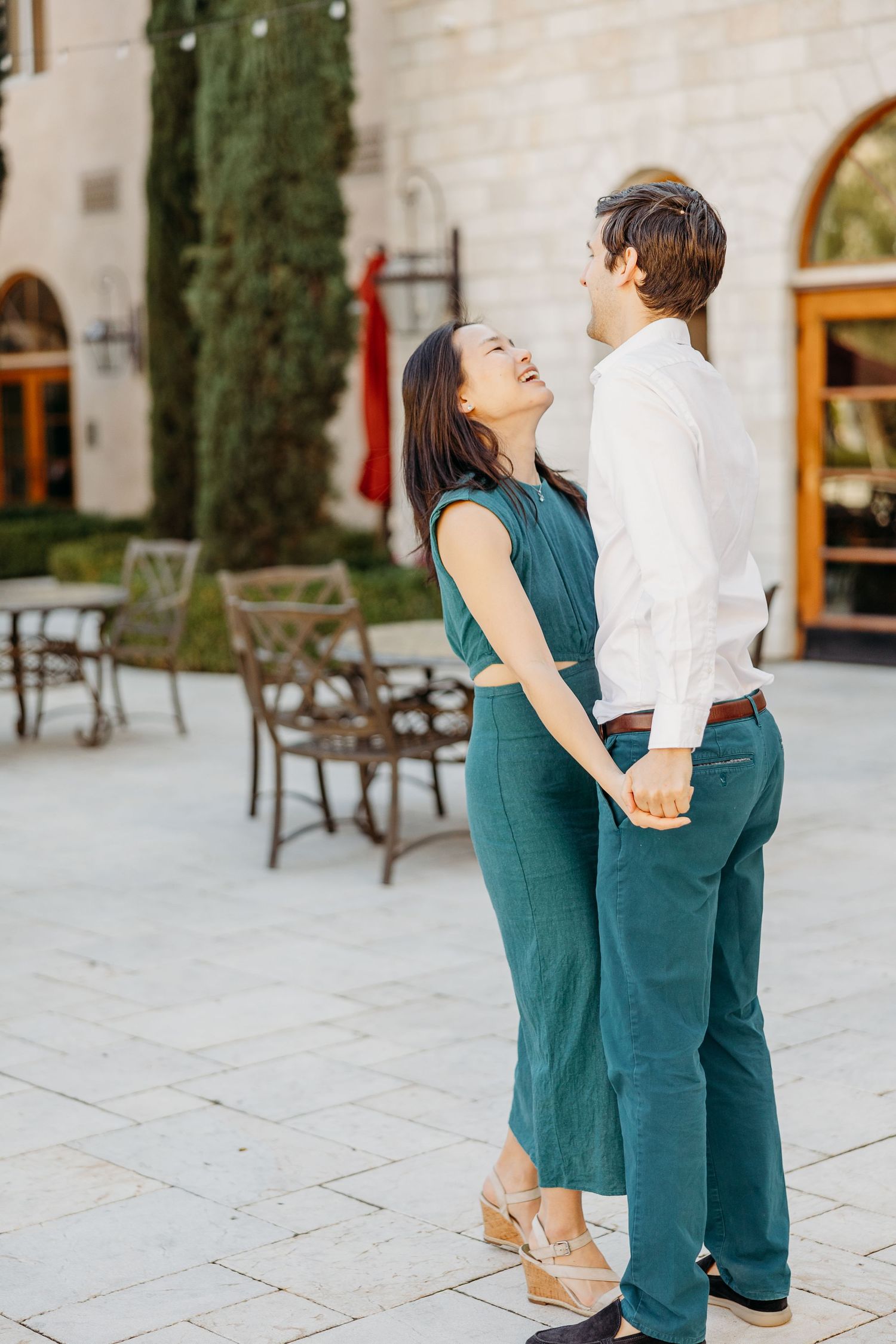 Couple in matching teal and white outfits embrace and laugh together on an elegant stone patio.