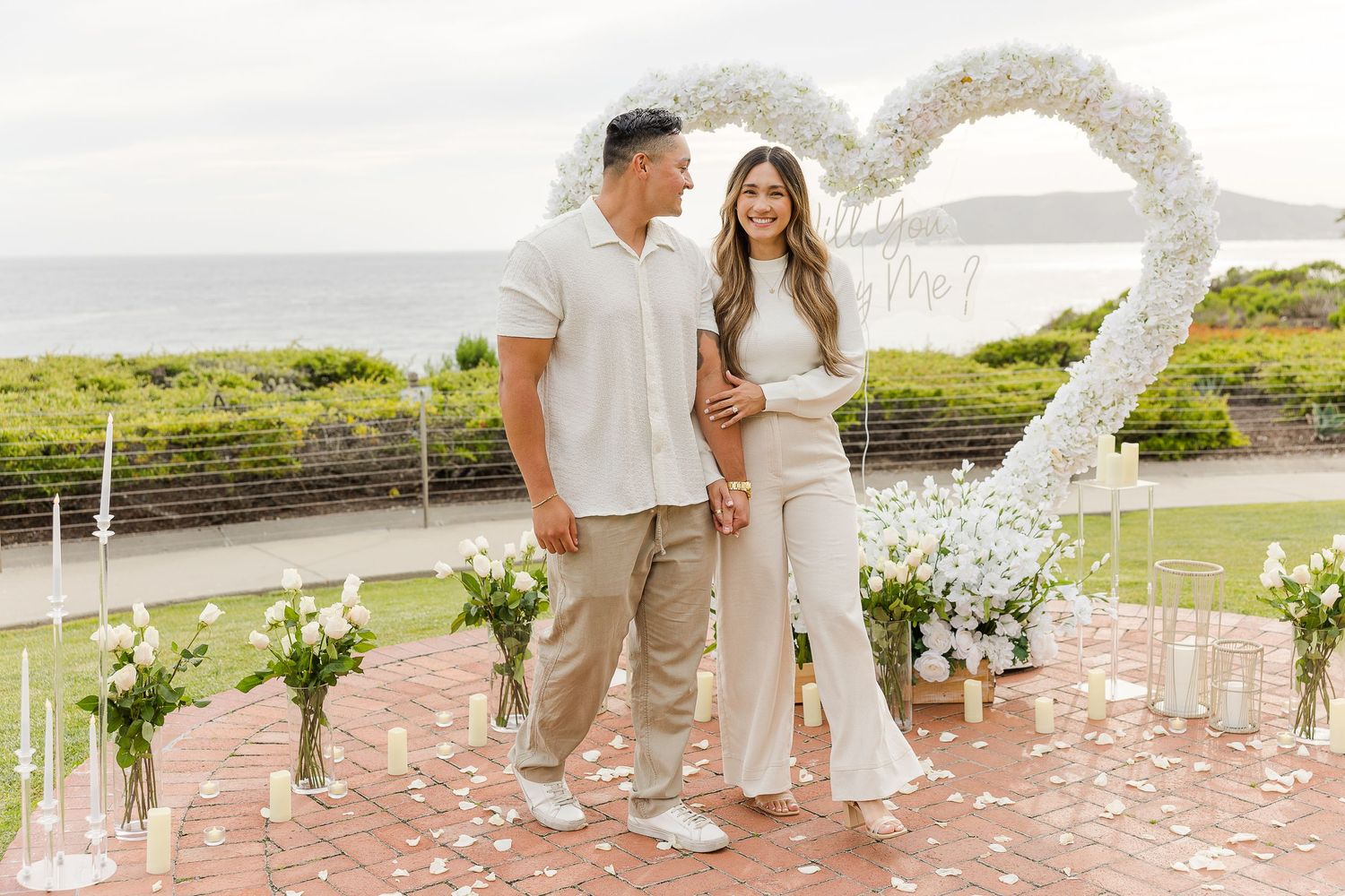 A floral wedding arch stands elegantly on a brick patio with guests gathered for a celebration.