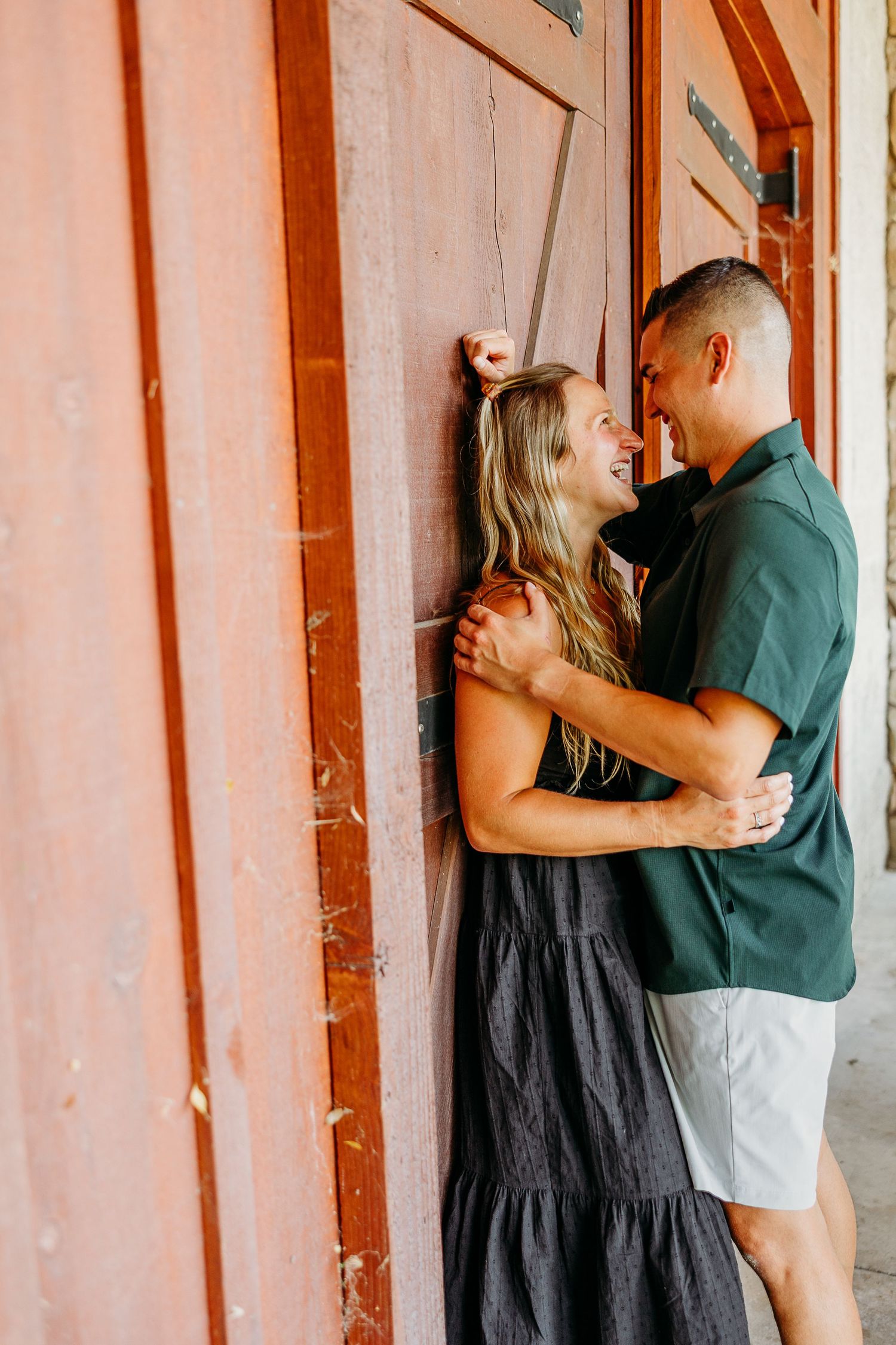 A couple embraces against a rustic wooden wall painted in warm tones.