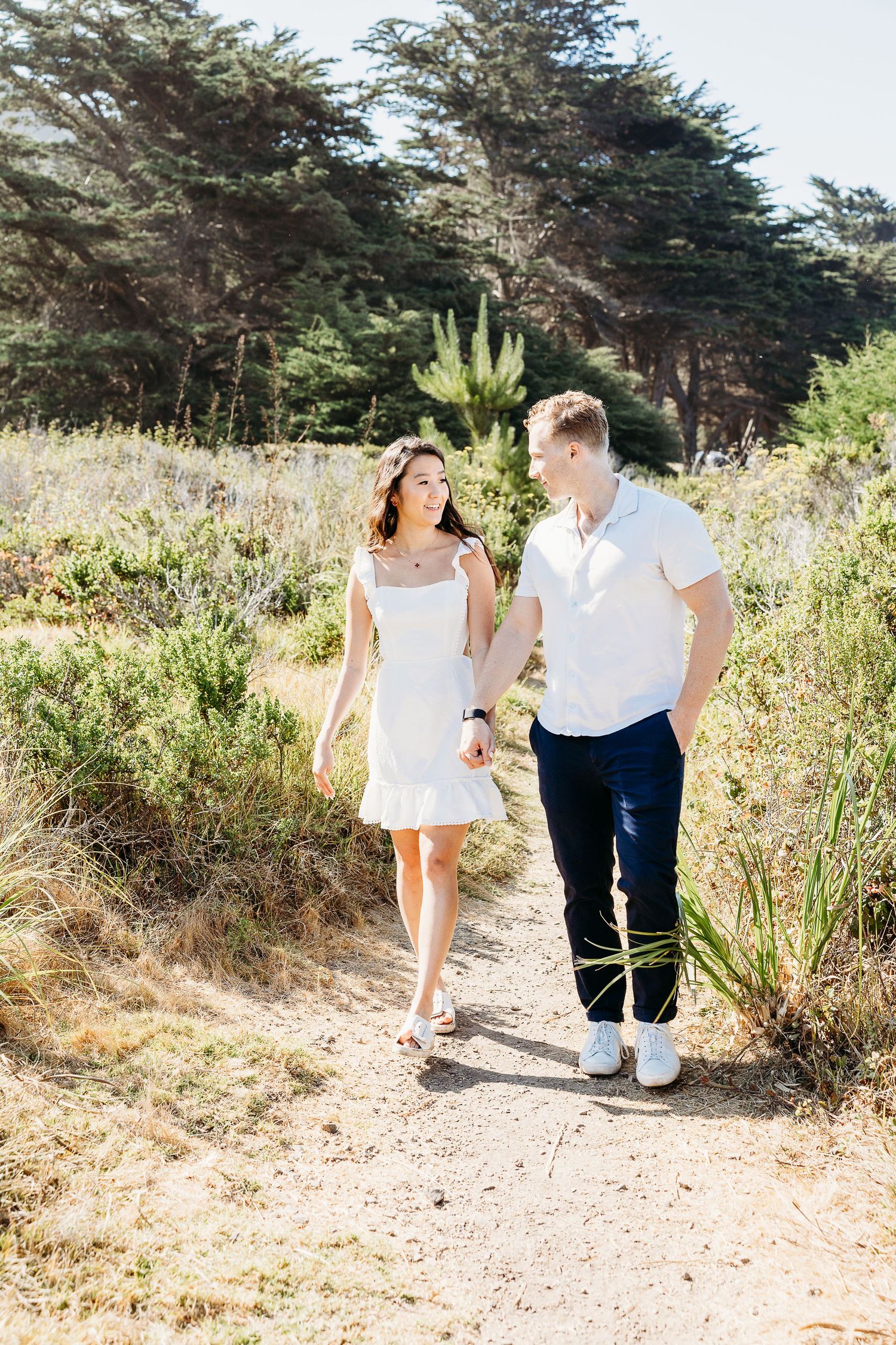 Couple walking together on nature trail surrounded by coastal vegetation.
