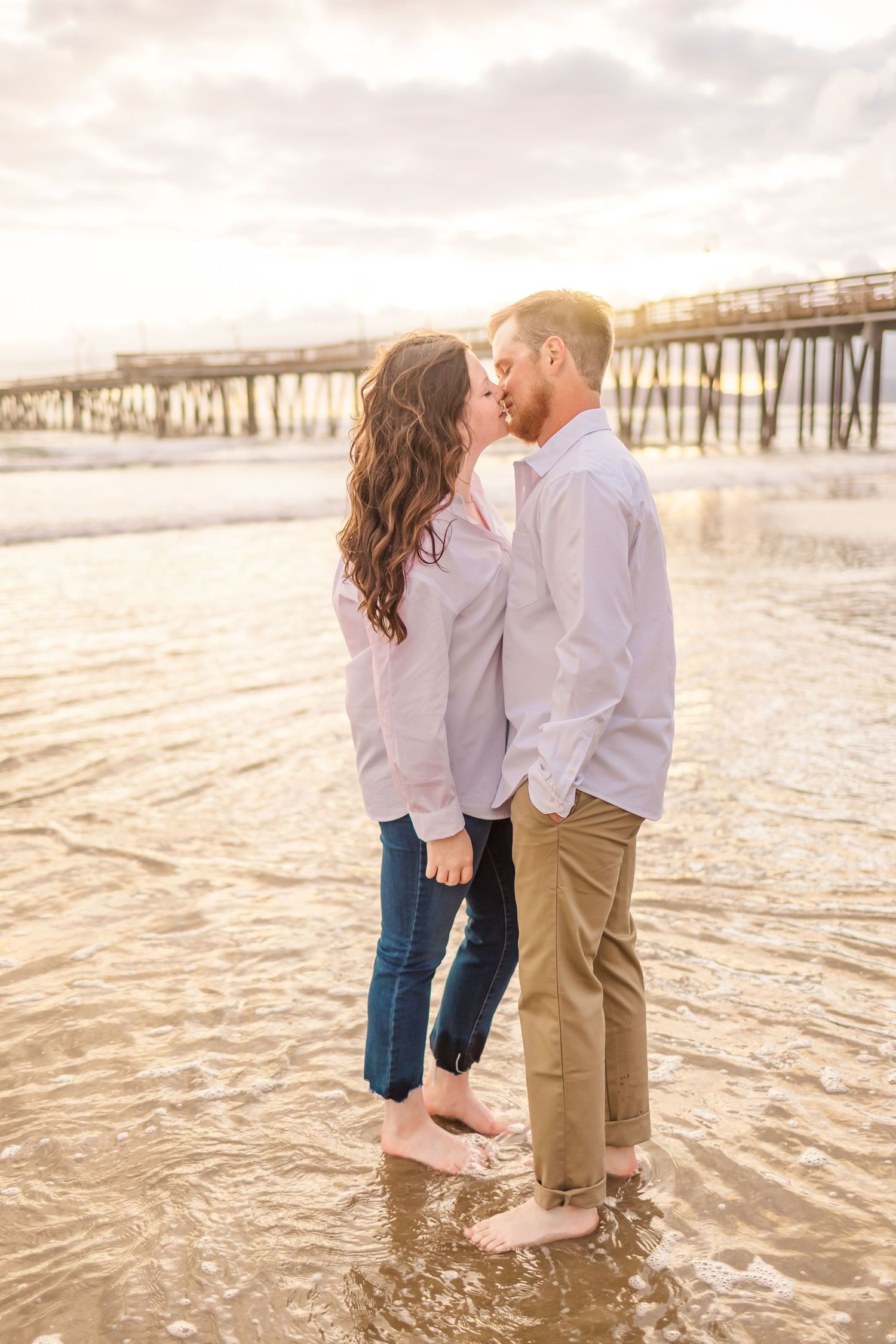 A romantic beach scene with couple standing in shallow water as waves lap at their feet.